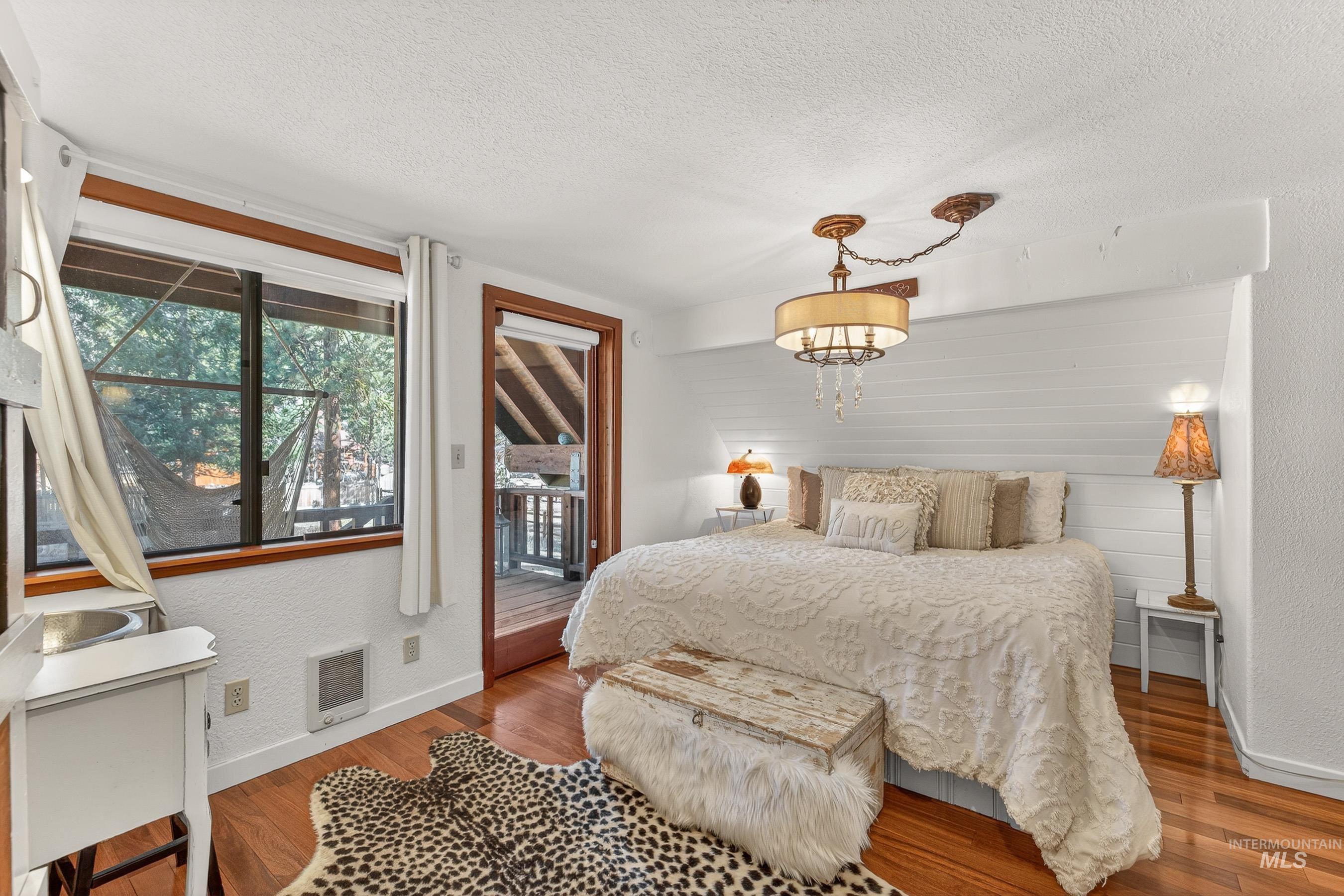 Hardwood-finish flooring anchors this room featuring a ceiling-mounted chandelier, shiplap accent wall, and a built-in wet bar