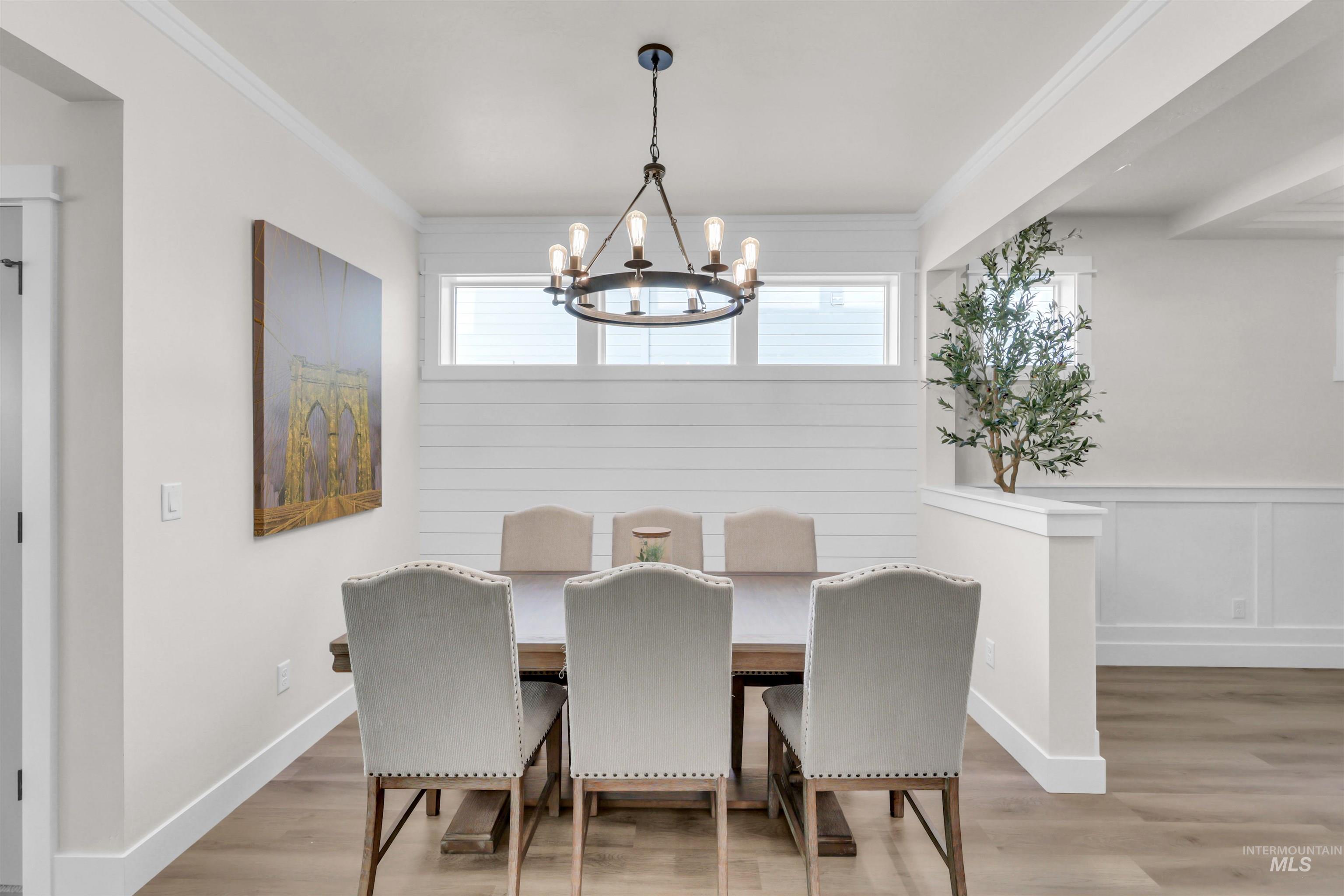 Dining area featuring light wood-style flooring, ornamental molding, a chandelier, and wainscoting