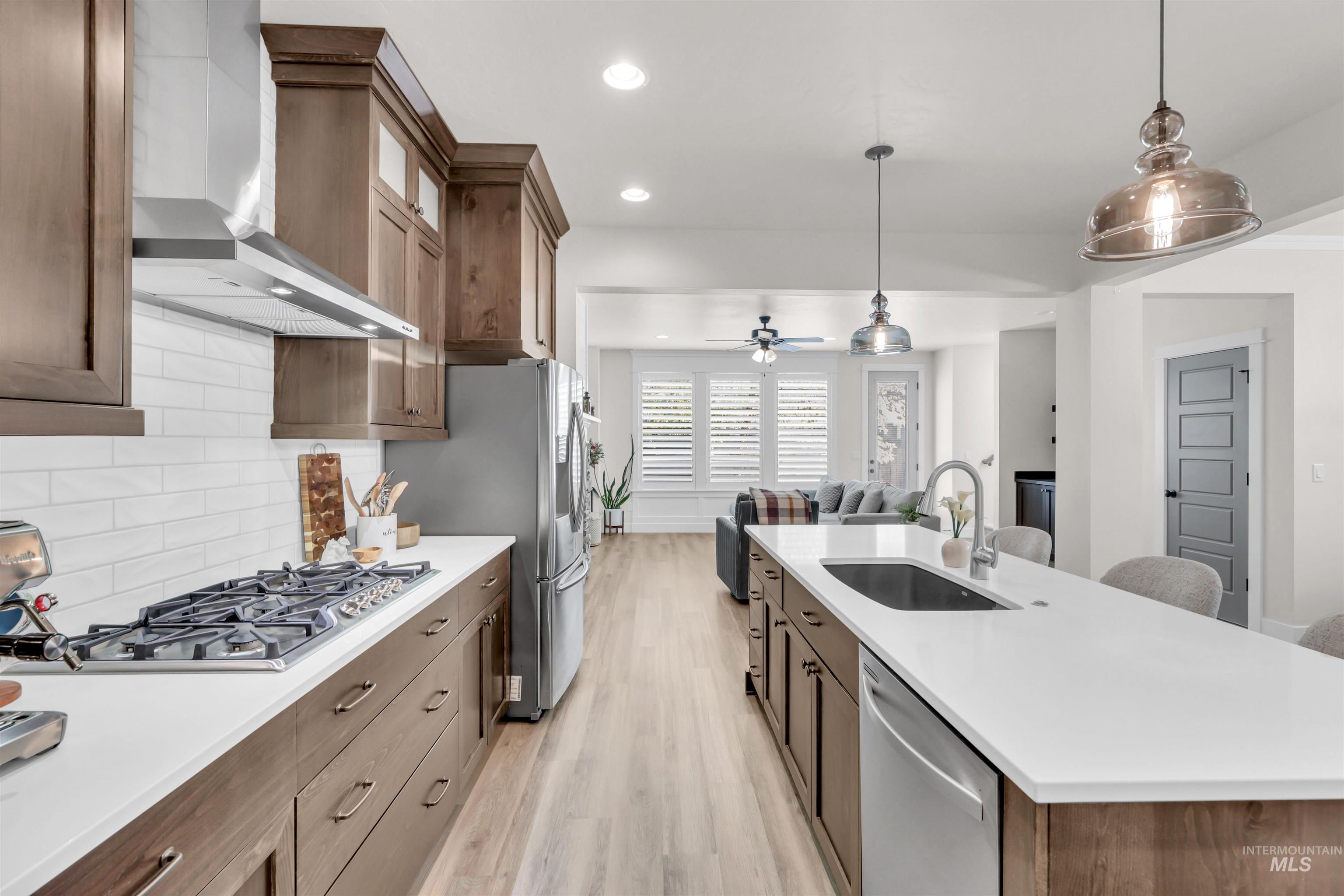 Kitchen with recessed lighting, pendant lighting, wall chimney exhaust hood, light wood finished floors, and brown cabinets