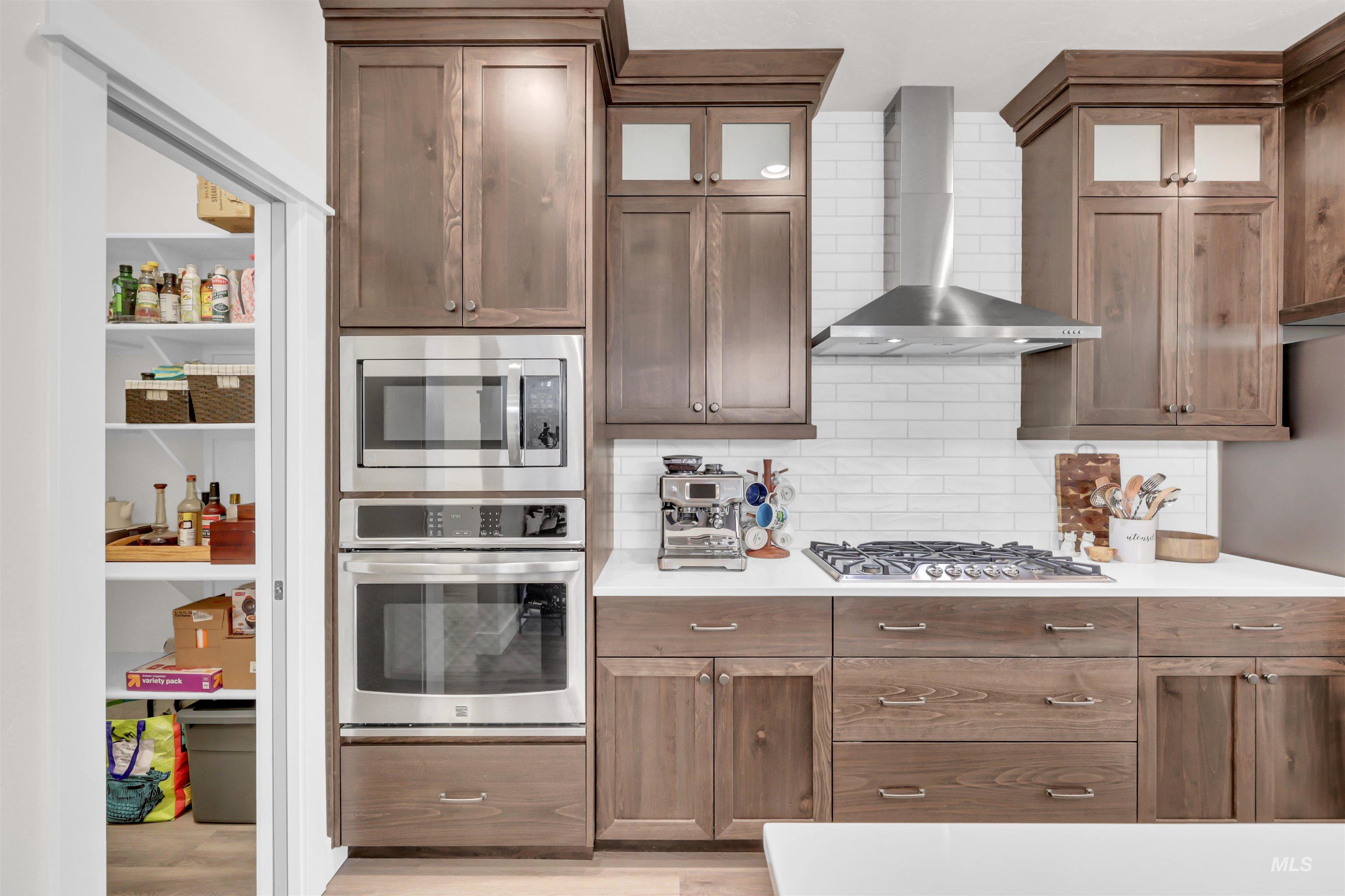 Kitchen featuring appliances with stainless steel finishes, wall chimney range hood, glass insert cabinets, tasteful backsplash, and light wood-style floors