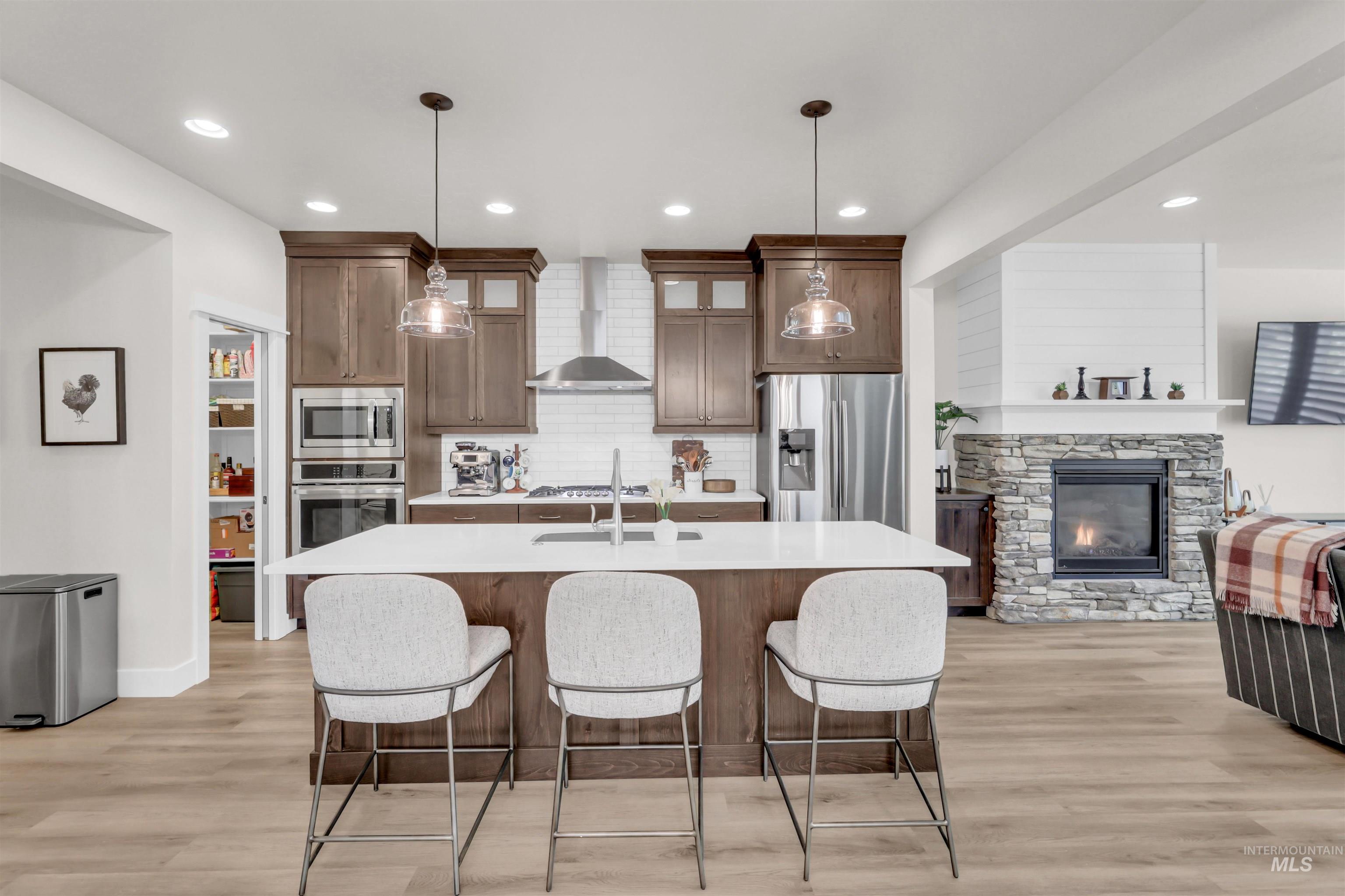 Kitchen featuring a fireplace, stainless steel appliances, light wood finished floors, wall chimney exhaust hood, and a kitchen breakfast bar