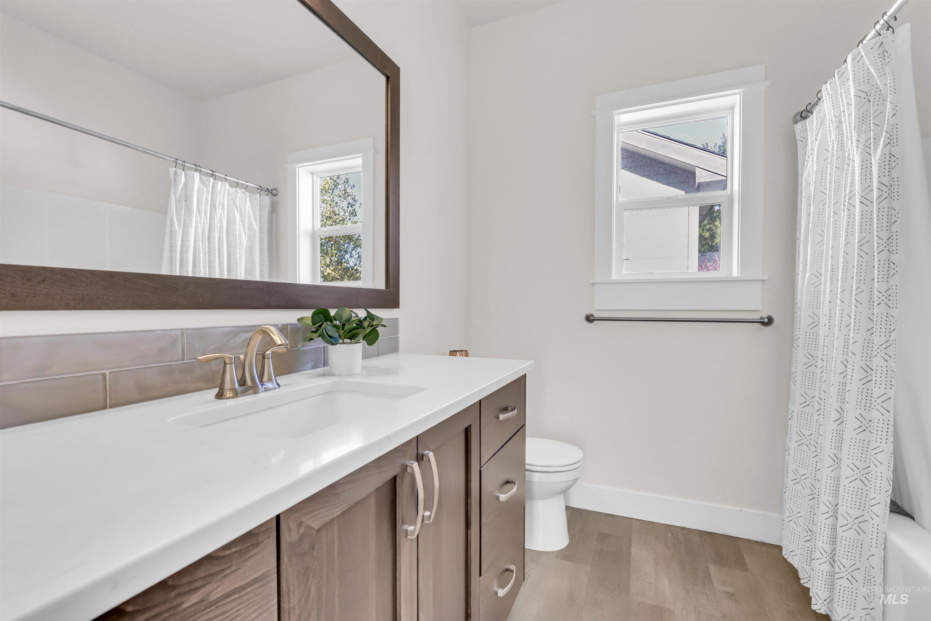 Bathroom featuring light wood-type flooring, healthy amount of natural light, vanity, and shower / tub combo with curtain