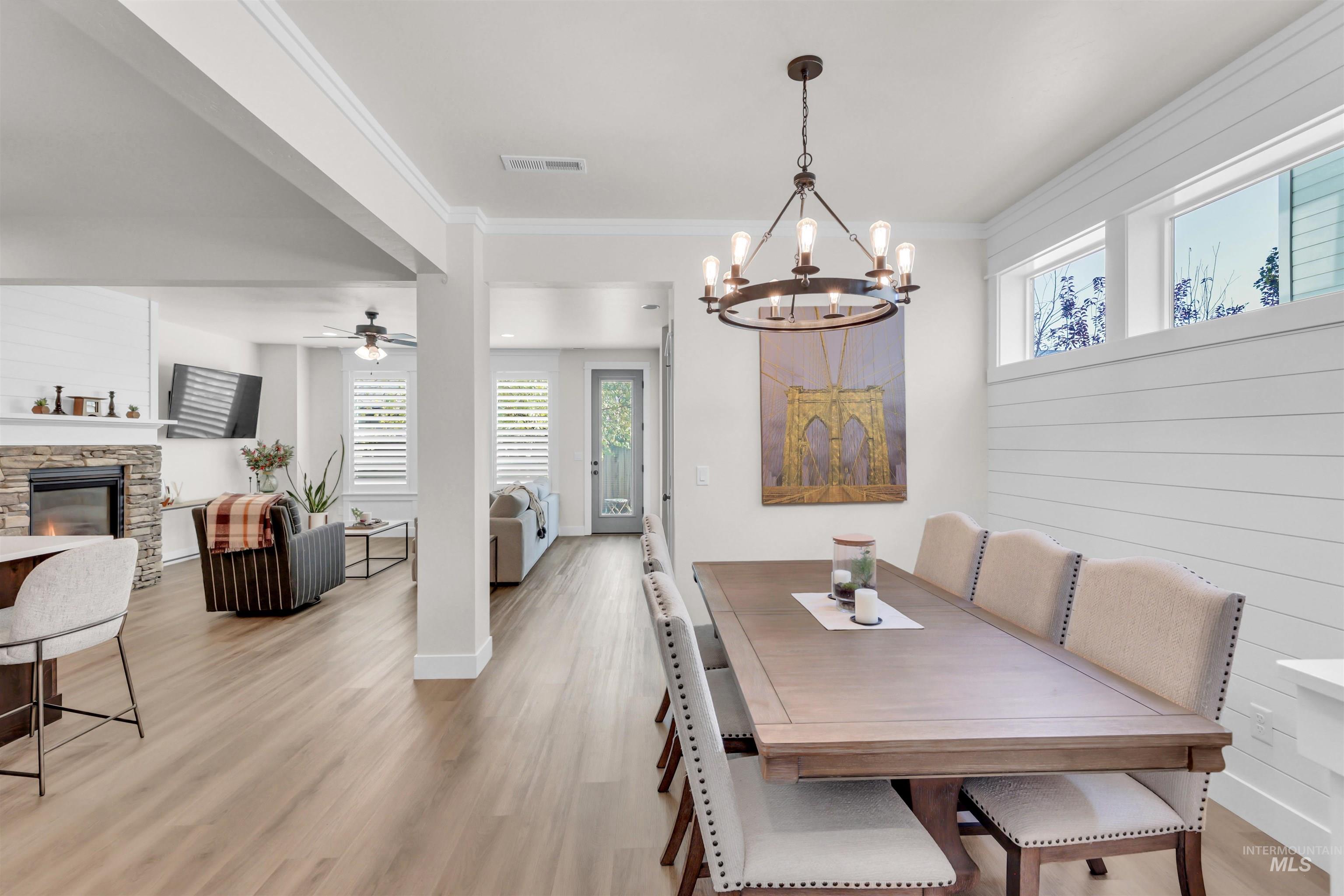 Dining room with light wood-style flooring, ornamental molding, a fireplace, a ceiling fan, and a chandelier