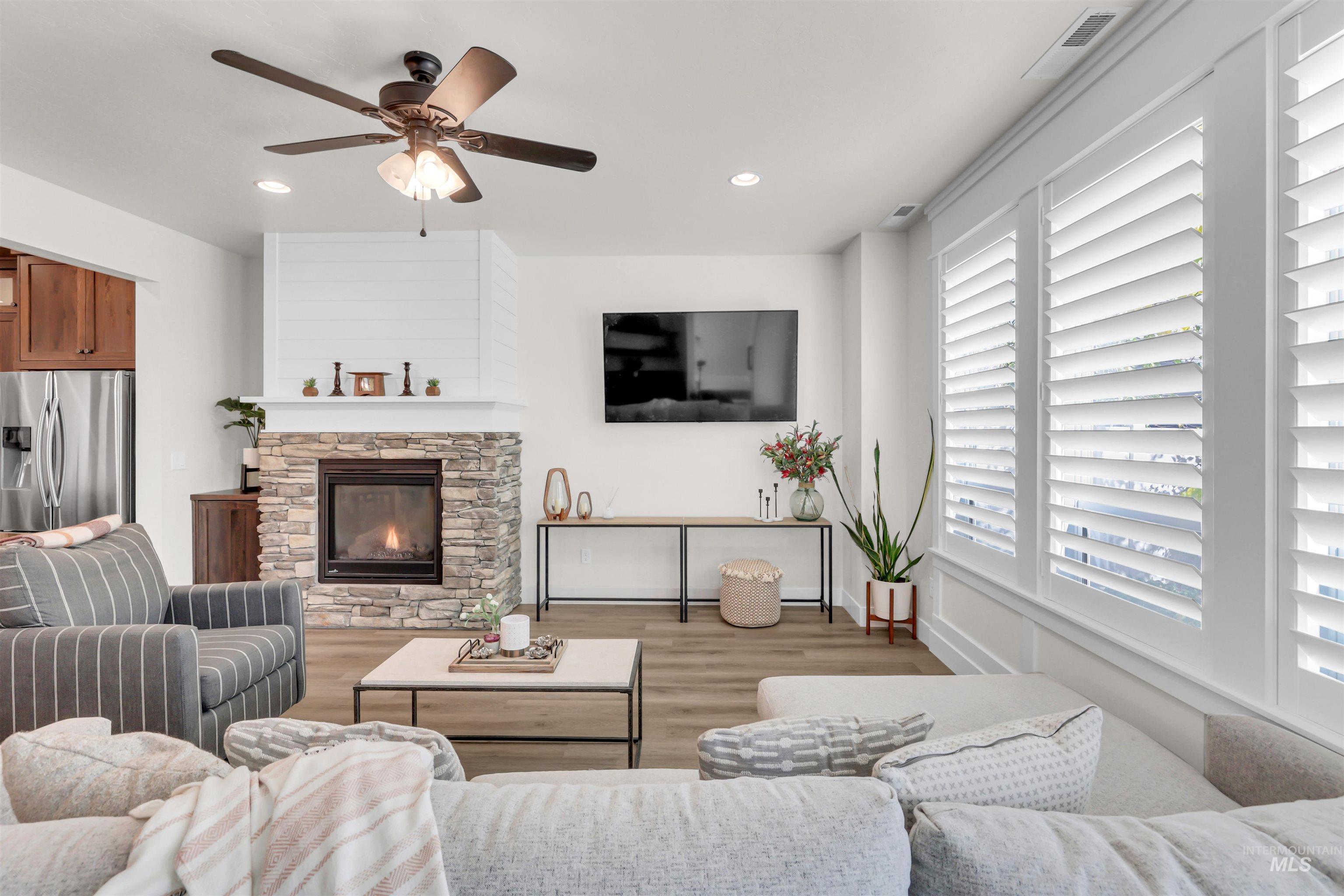 Living room featuring wood finished floors, recessed lighting, a stone fireplace, and a ceiling fan
