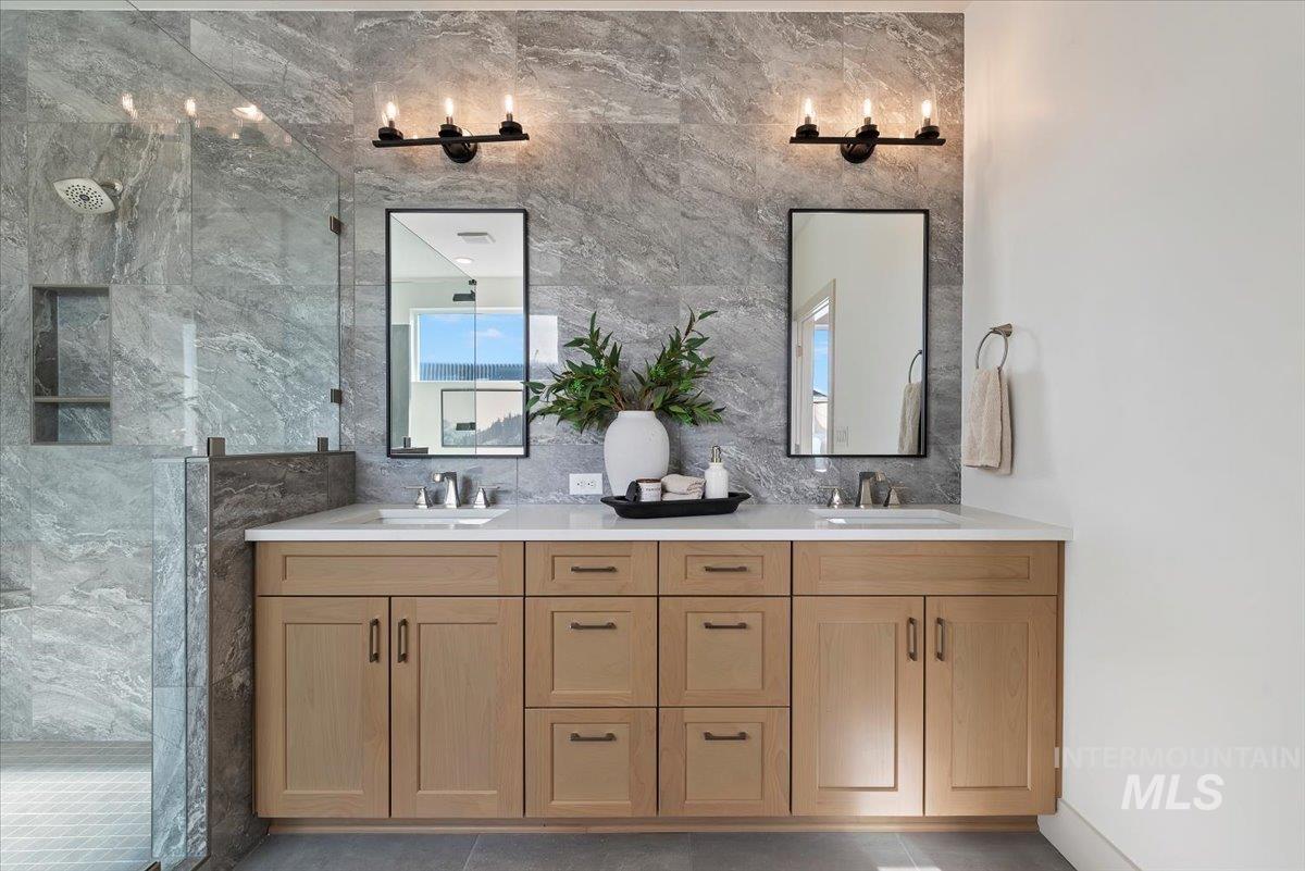 Full bath featuring double vanity, a marble finish shower, light tile patterned flooring, and tile walls