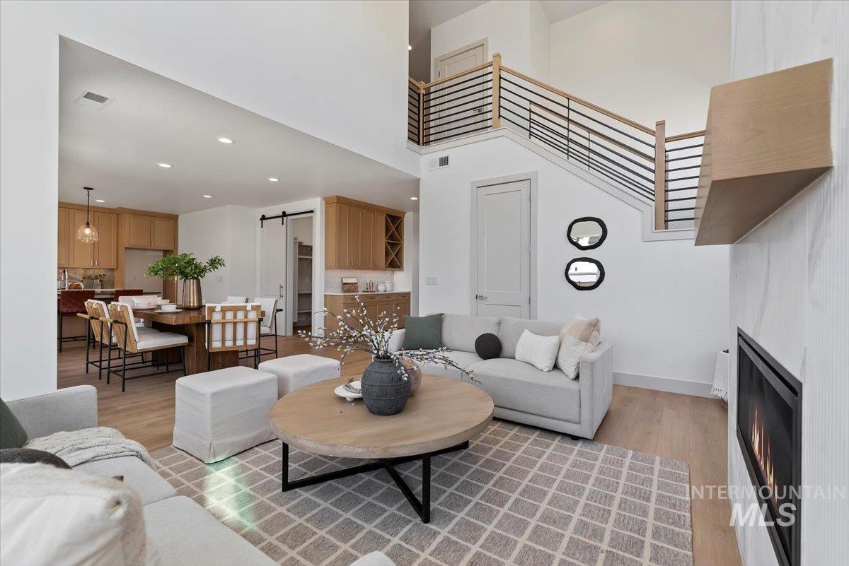 Living room with a barn door, light wood-style floors, a warm lit fireplace, a high ceiling, and recessed lighting