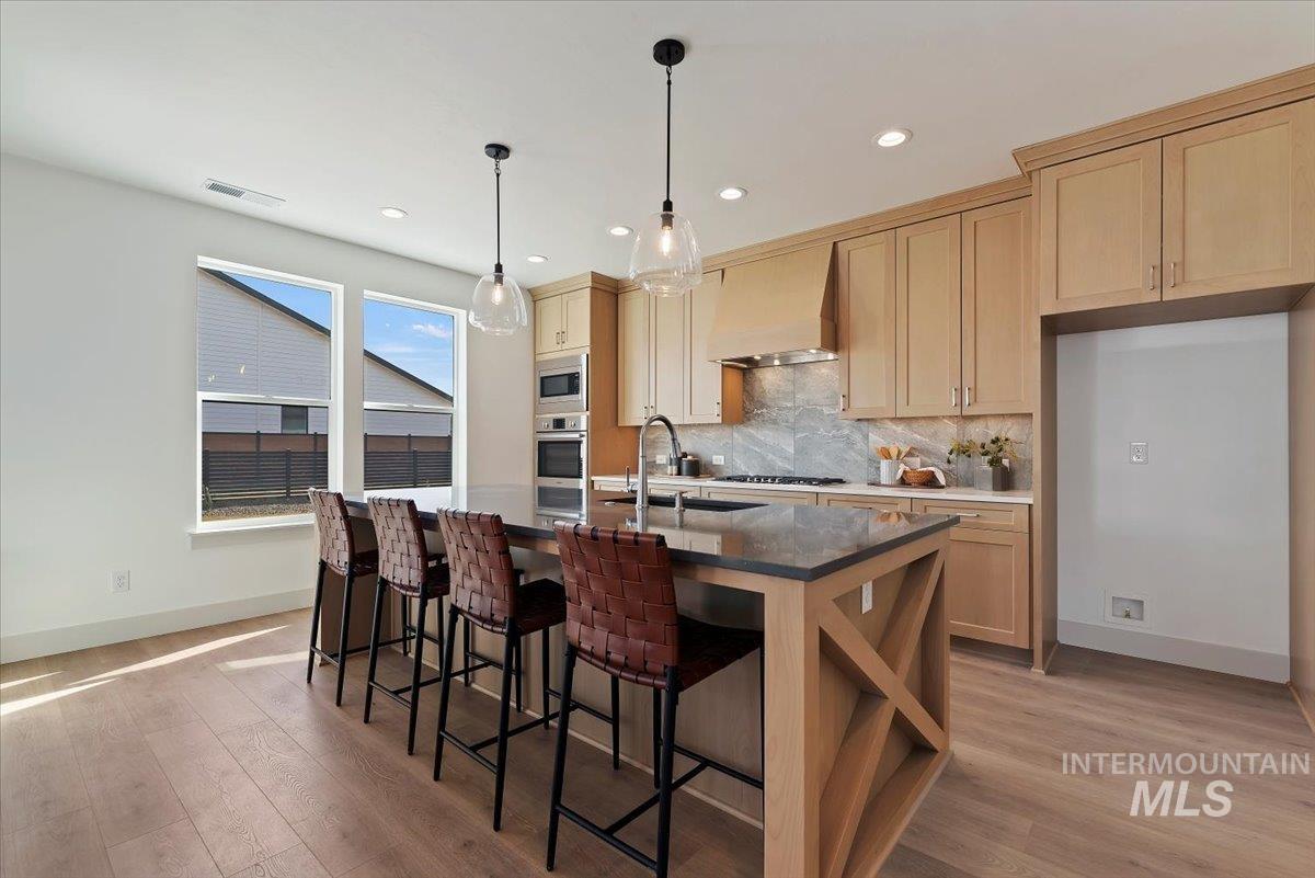Kitchen with light wood finished floors, a kitchen bar, an island with sink, and light wood finish cabinetry