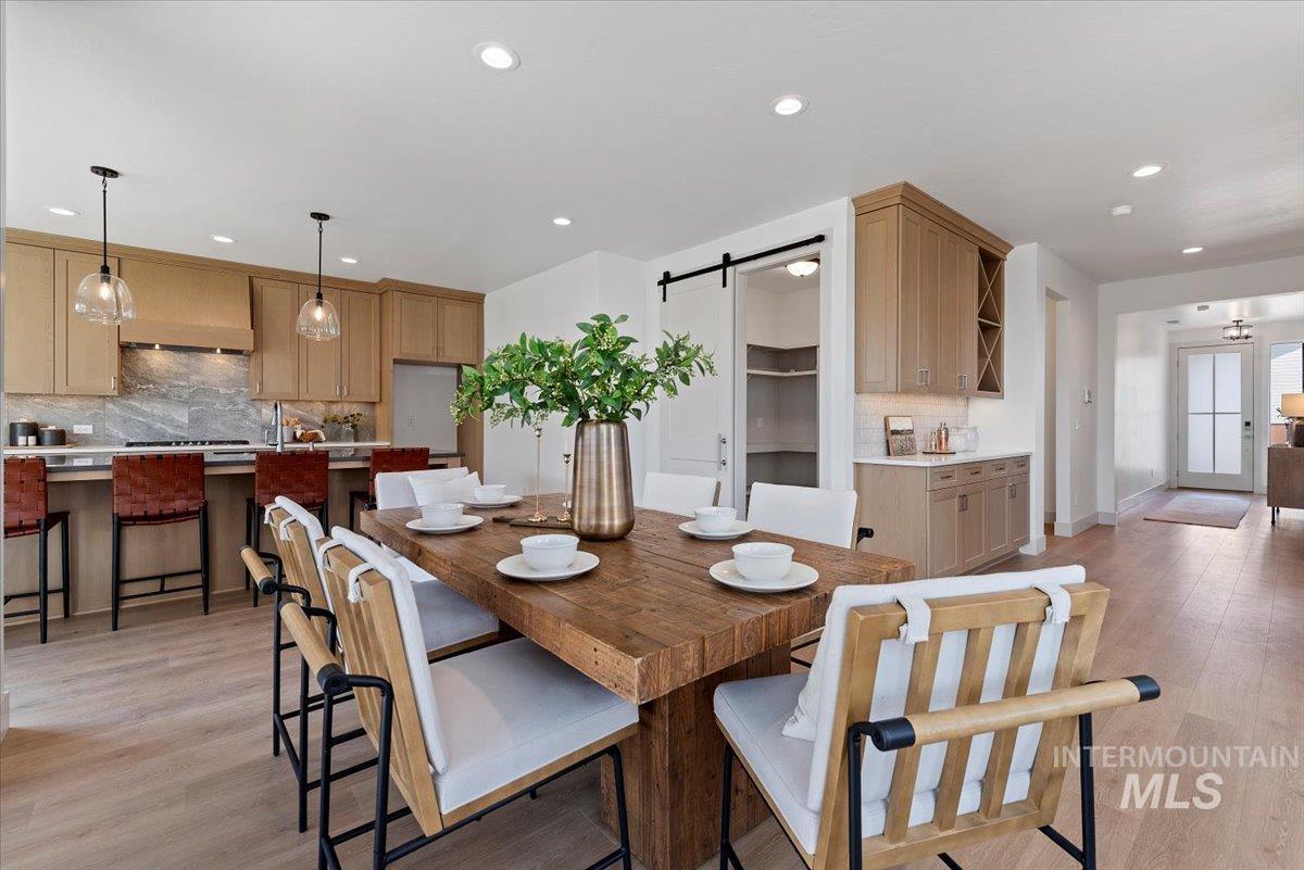 Dining room with a barn door, light wood finished floors, and recessed lighting