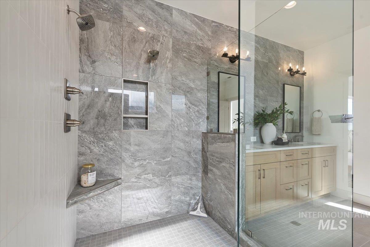 Bathroom with a marble finish shower, double vanity, and light tile patterned floors