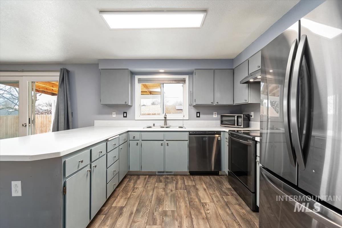 Kitchen with gray cabinetry, appliances with stainless steel finishes, light countertops, a peninsula, and dark wood-type flooring