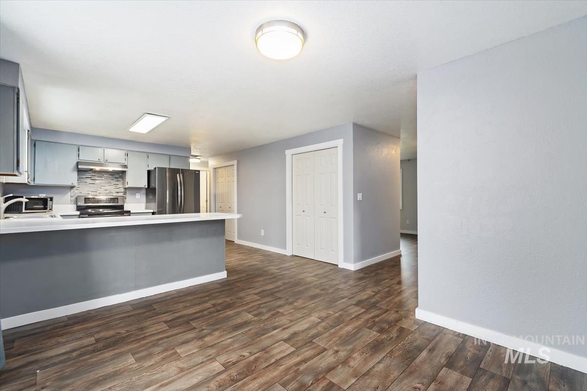 Kitchen with light countertops, stainless steel appliances, gray cabinetry, backsplash, and dark wood finished floors