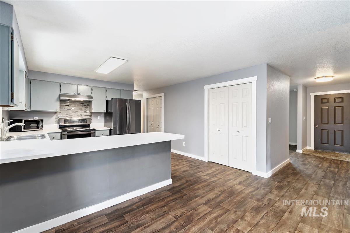 Kitchen featuring gray cabinets, stainless steel appliances, light countertops, dark wood-style flooring, and a peninsula