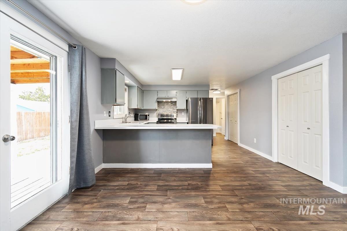 Kitchen featuring gray cabinetry, light countertops, stainless steel appliances, a peninsula, and dark wood-style floors