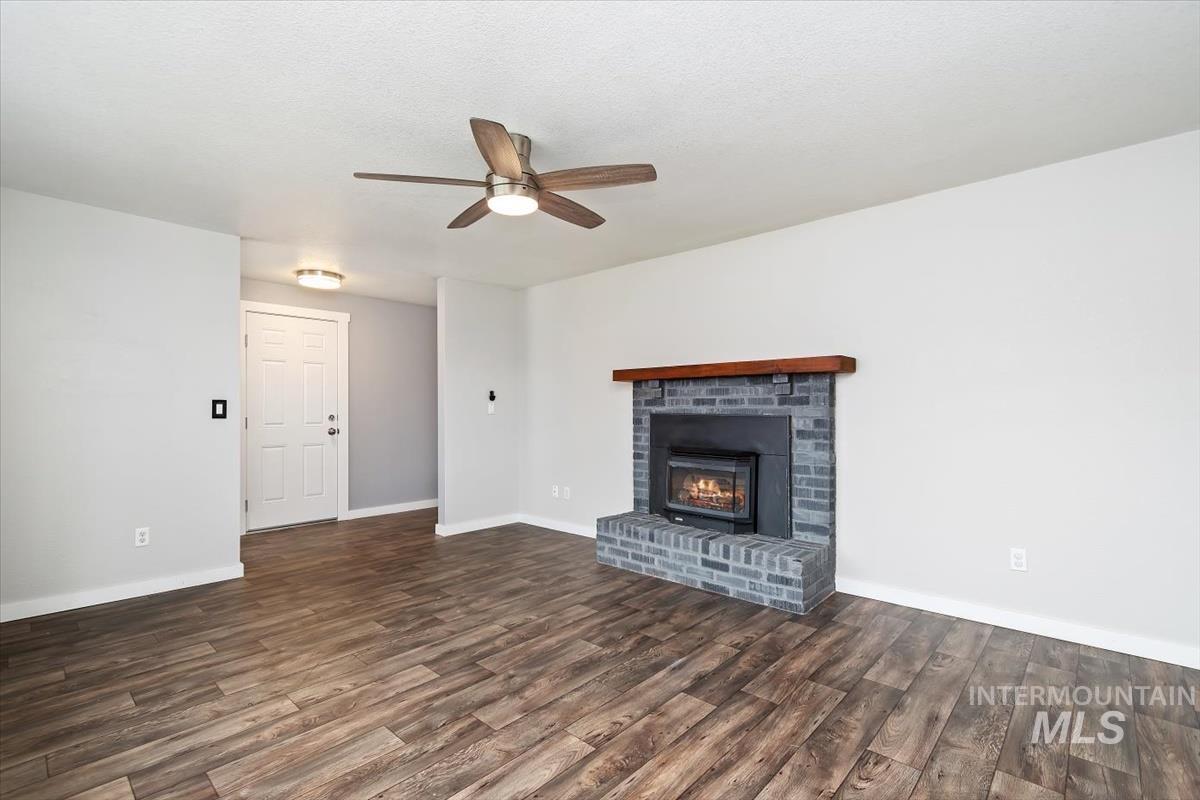 Unfurnished living room with a fireplace, dark wood-type flooring, and a ceiling fan