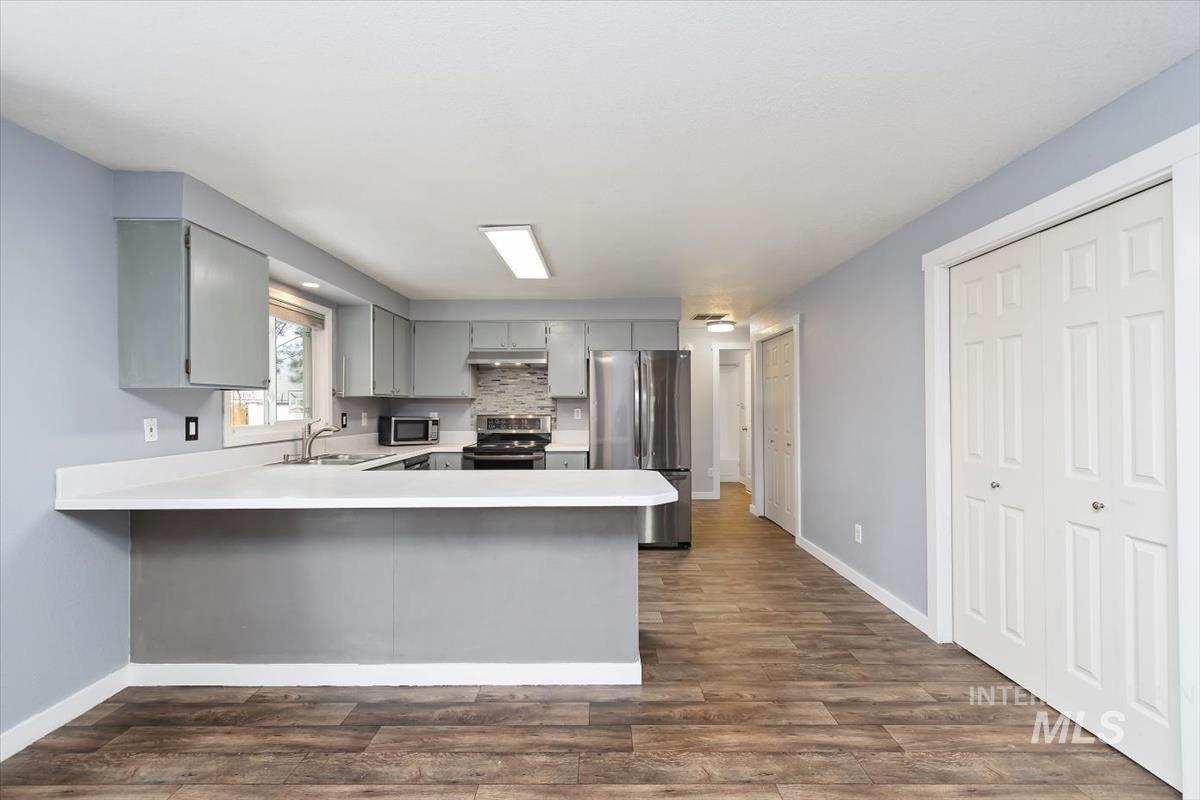 Kitchen with light countertops, gray cabinets, stainless steel appliances, a peninsula, and dark wood-type flooring