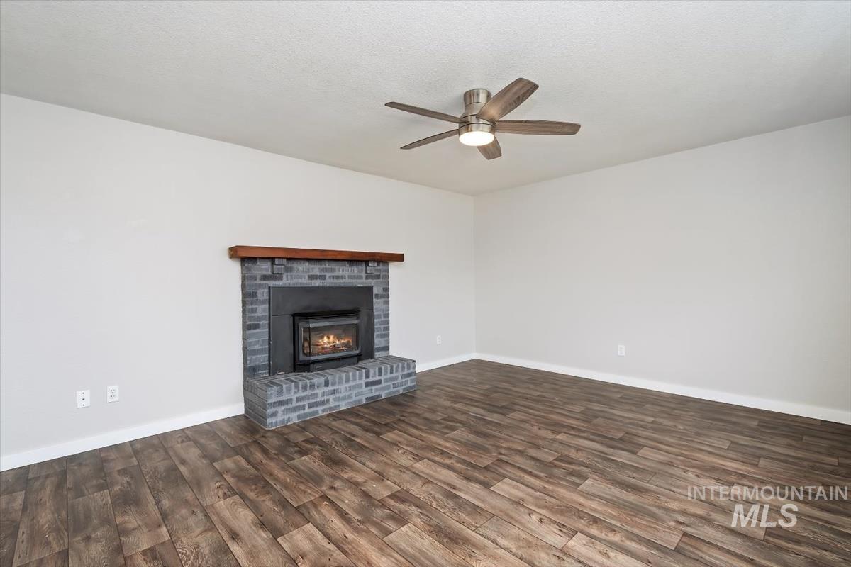 Unfurnished living room featuring a ceiling fan, dark wood-style flooring, a brick fireplace, and a textured ceiling