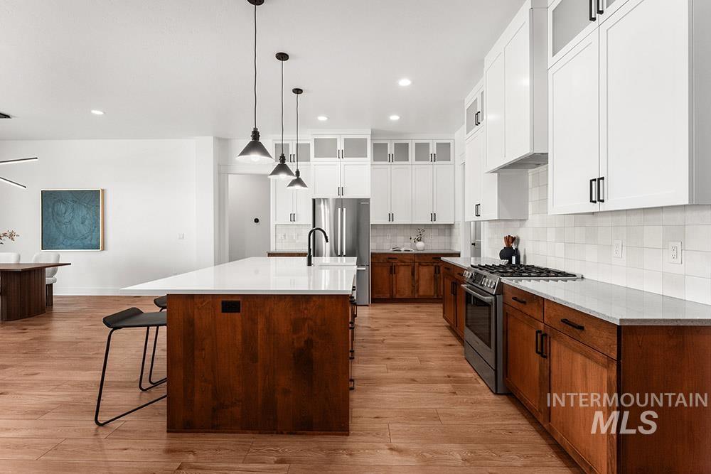Kitchen with stainless steel appliances, glass insert cabinets, light wood-style floors, light countertops, and a kitchen breakfast bar