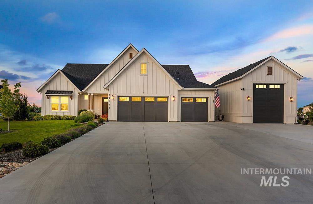 Modern farmhouse style home featuring board and batten siding, roof with shingles, a garage, a front yard, and driveway