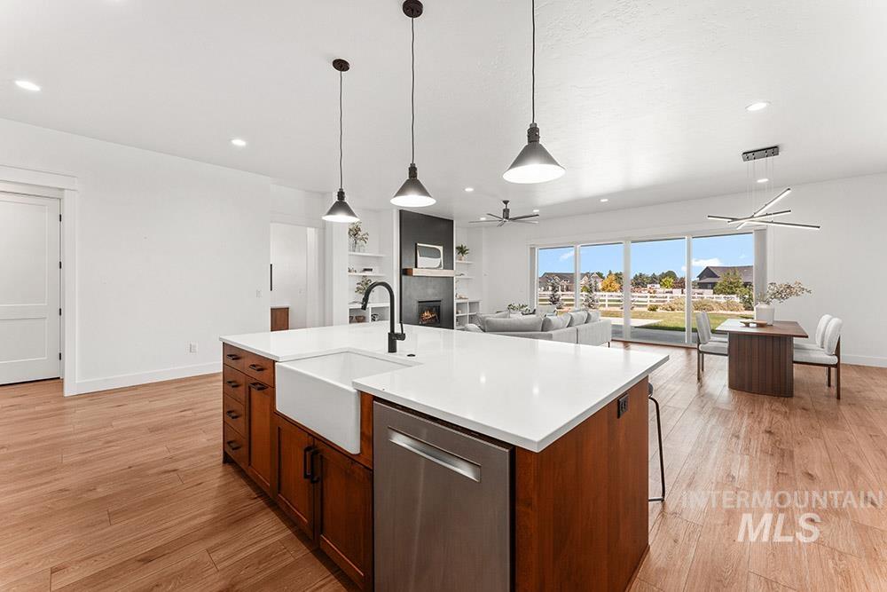 Kitchen featuring dishwasher, ceiling fan, a warm lit fireplace, light countertops, and light wood finished floors