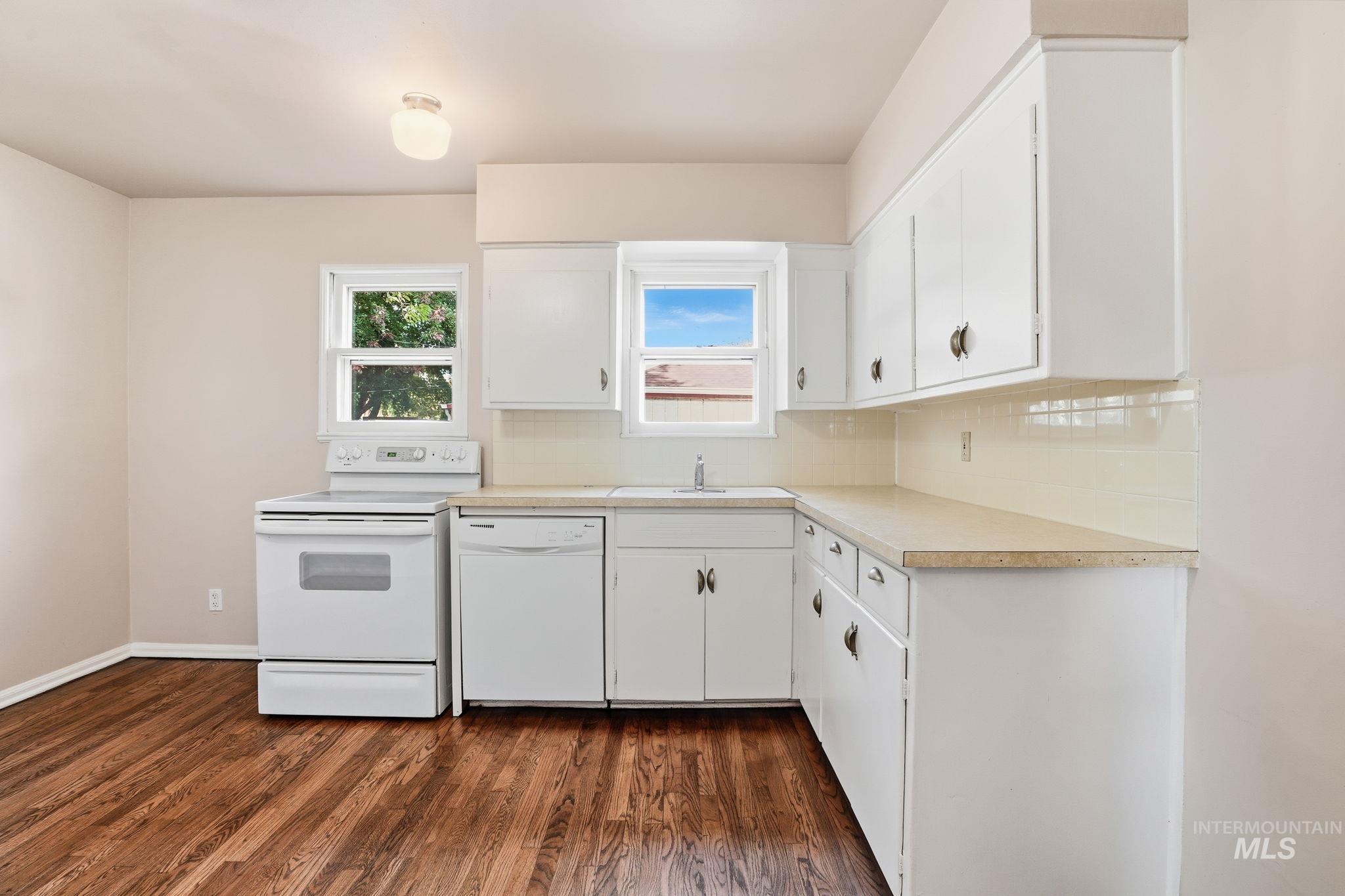 Kitchen featuring white appliances, light countertops, white cabinetry, dark wood finished floors, and tasteful backsplash