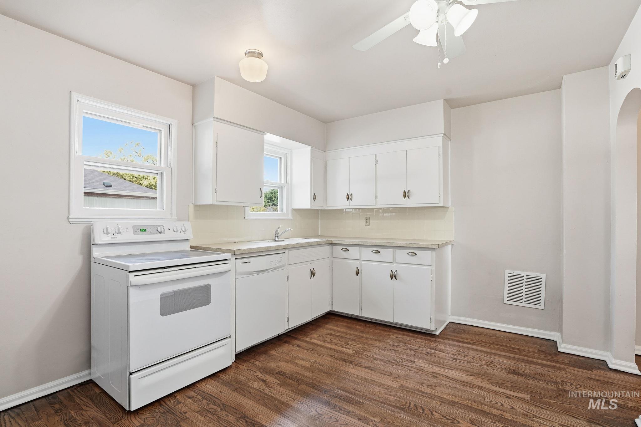 Kitchen with white appliances, light countertops, arched walkways, and white cabinets