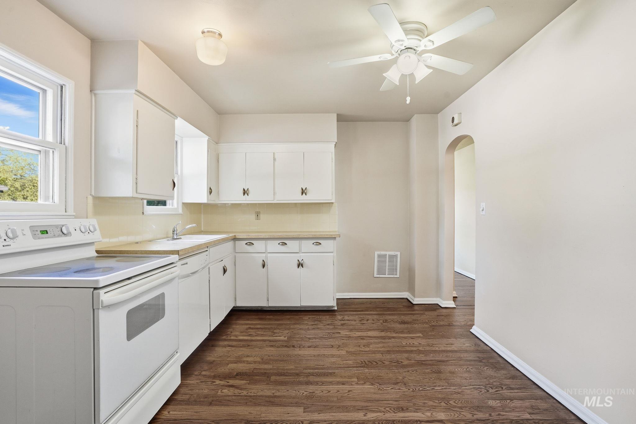 Kitchen featuring white appliances, light countertops, dark wood-type flooring, white cabinetry, and arched walkways