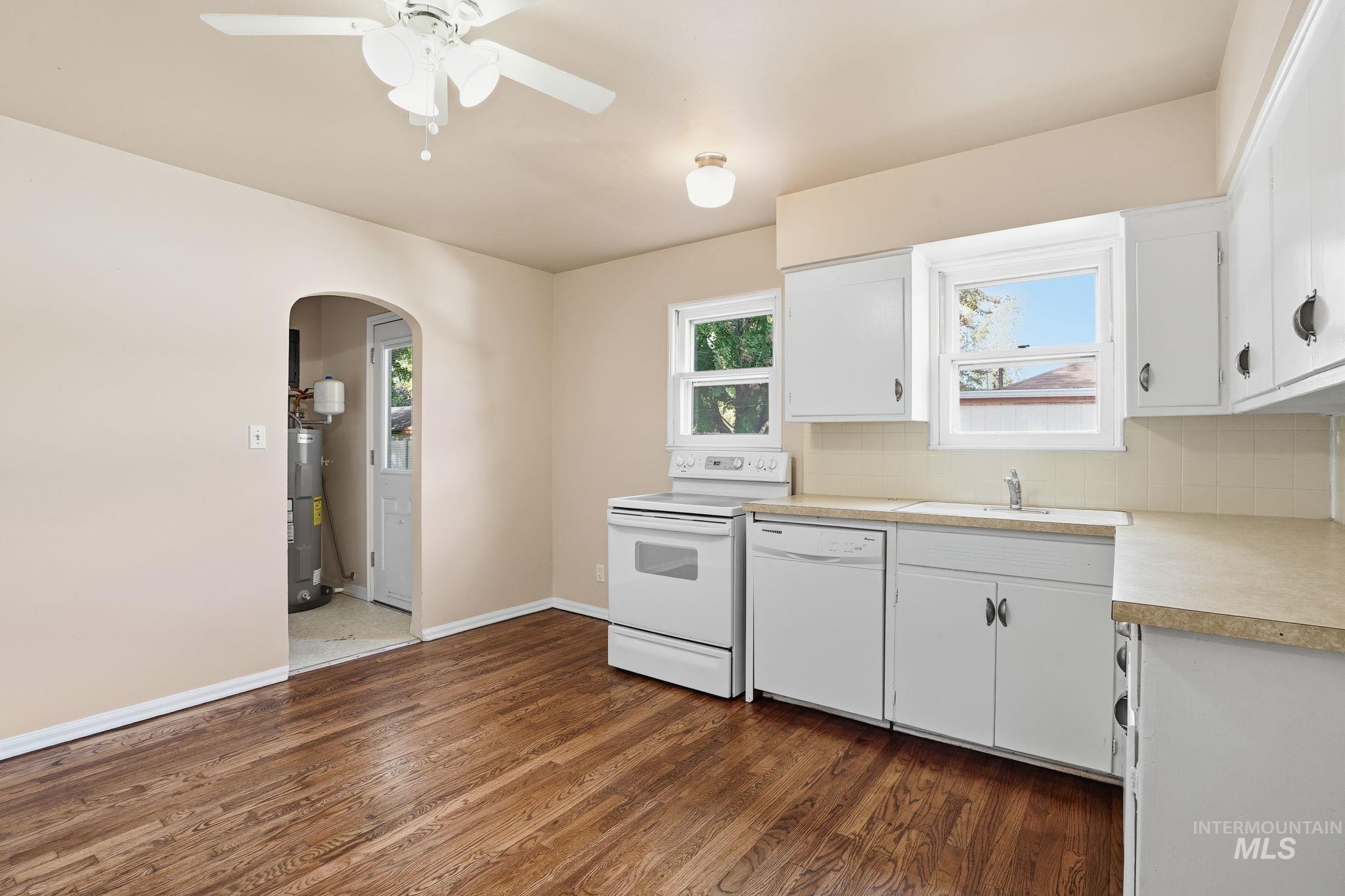 Kitchen with white cabinetry, white appliances, arched walkways, and light countertops