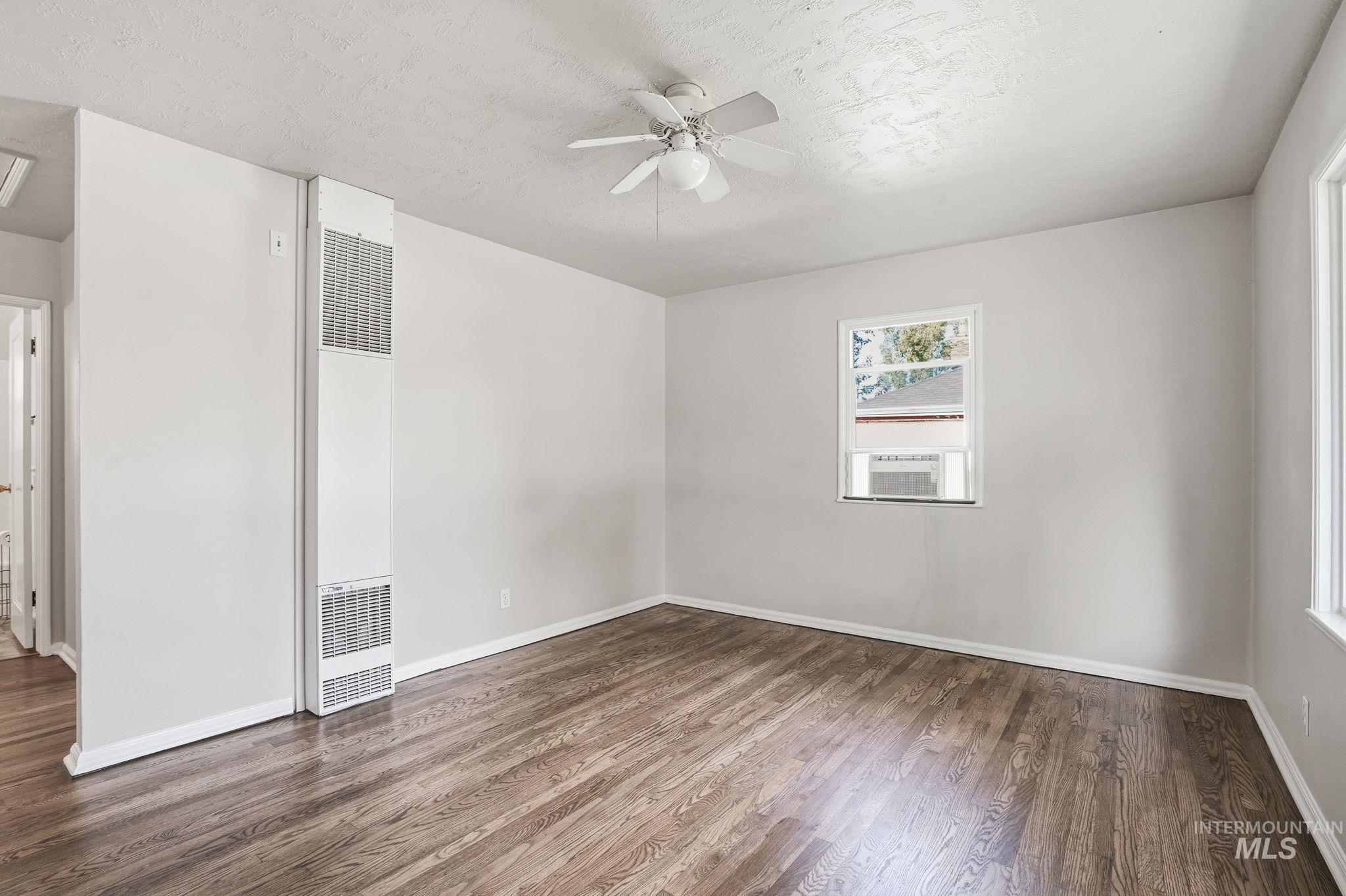 Spare room with dark wood-type flooring, a heating unit, a textured ceiling, and a ceiling fan