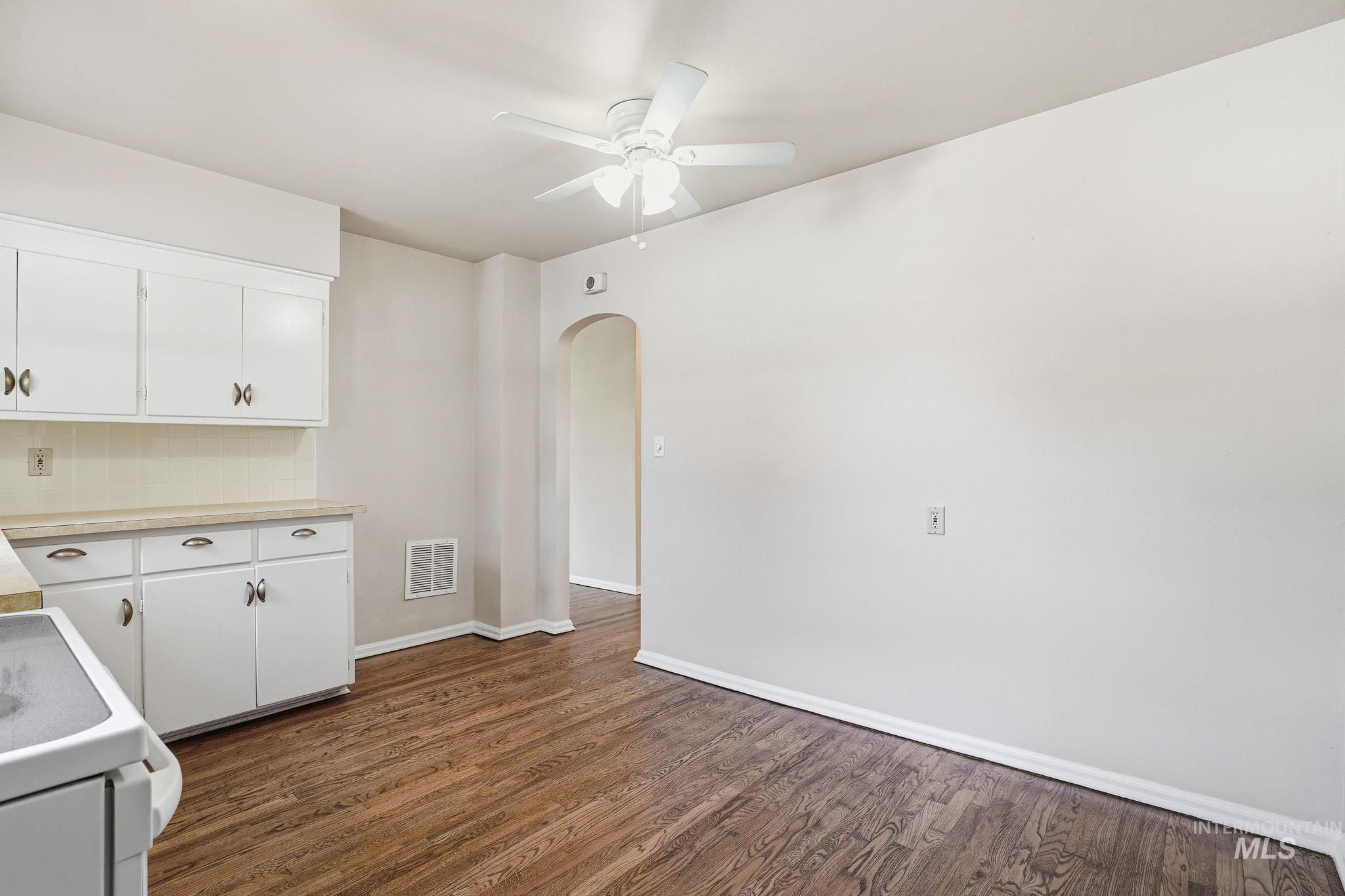 Kitchen featuring light countertops, white stove, arched walkways, dark wood finished floors, and white cabinets
