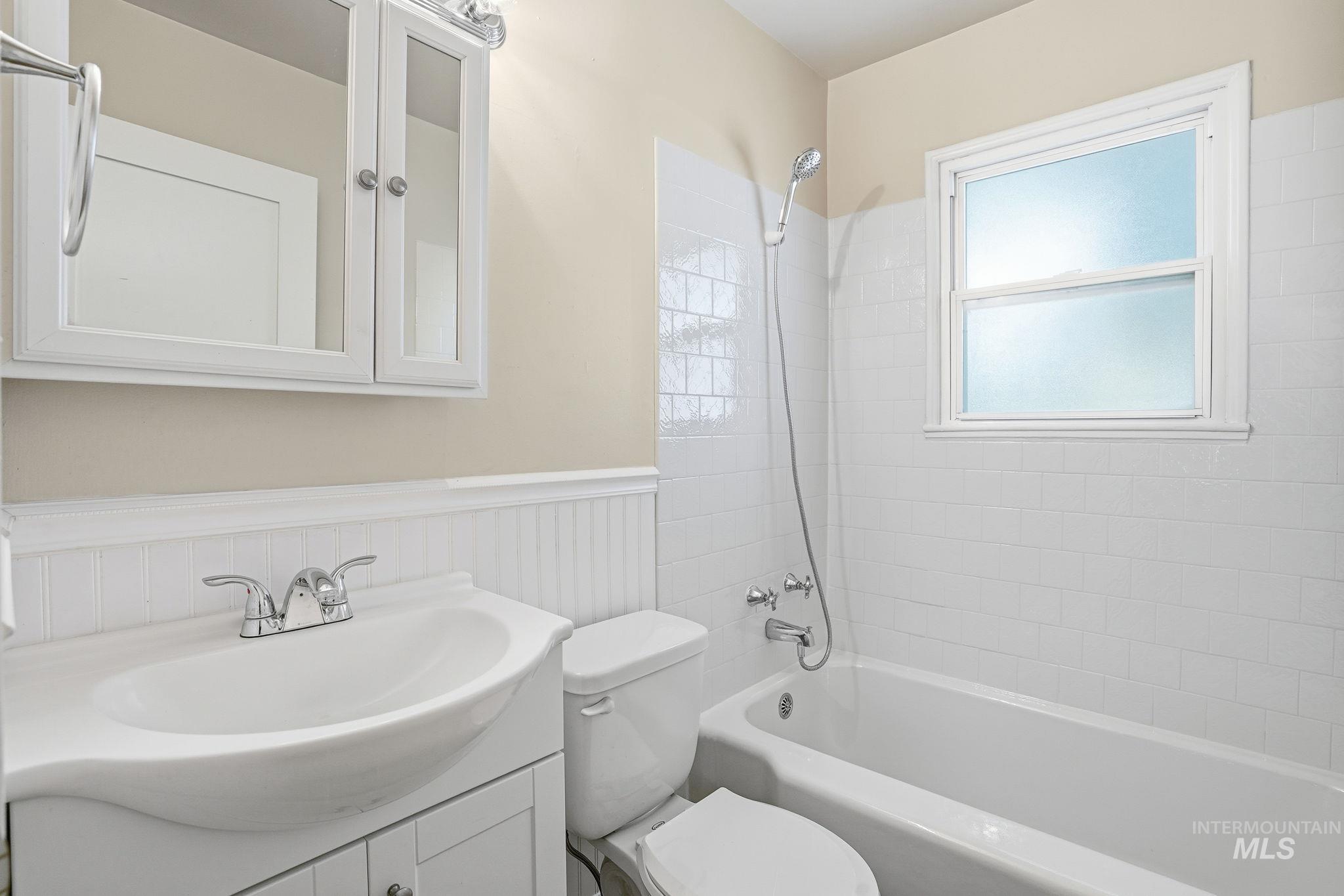 Bathroom featuring tub / shower combination, vanity, and wainscoting