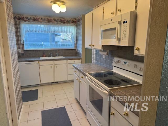Kitchen featuring white appliances, white cabinetry, light tile patterned floors, and decorative backsplash