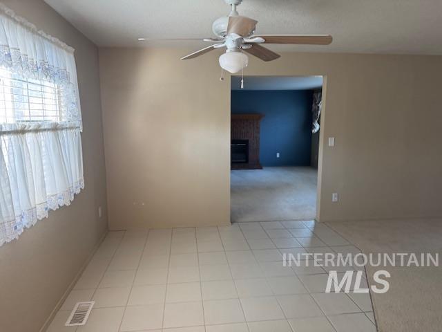 Spare room featuring light colored carpet, light tile patterned floors, ceiling fan, and a fireplace
