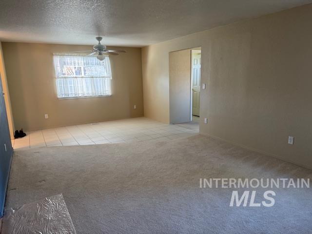 Unfurnished room featuring a textured ceiling, light carpet, and ceiling fan