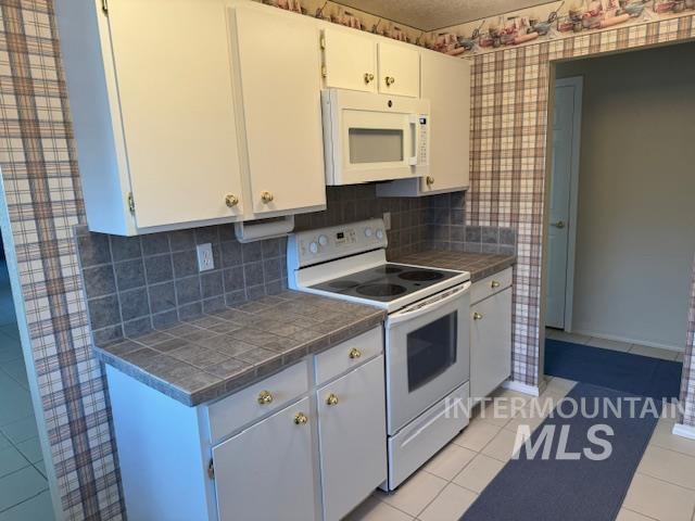 Kitchen featuring tile countertops, white appliances, white cabinets, decorative backsplash, and light tile patterned floors