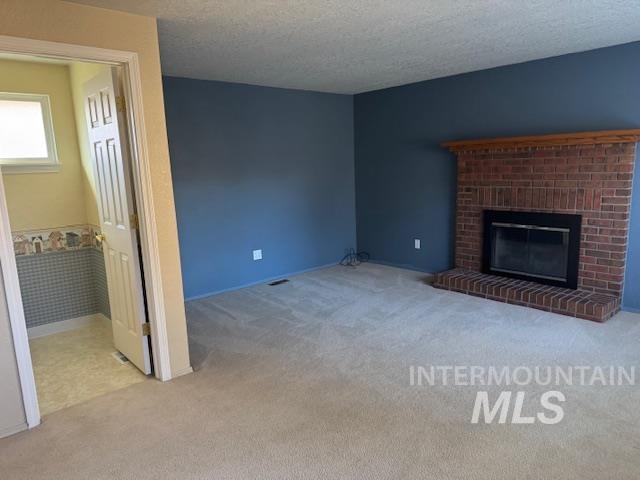 Unfurnished living room featuring light colored carpet, a fireplace, and a textured ceiling
