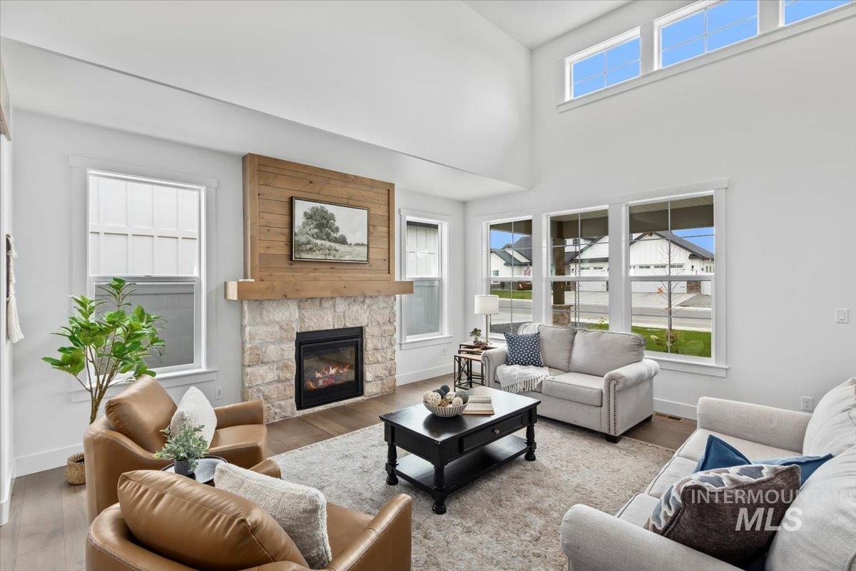 Living room with a stone fireplace, wood finished floors, and a high ceiling