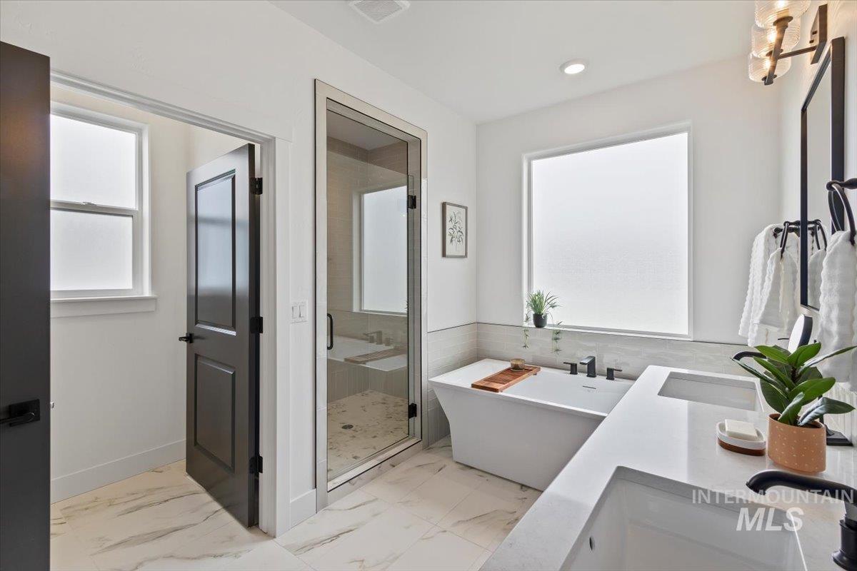 Full bathroom featuring a soaking tub, a stall shower, double vanity, and light marble finish floors