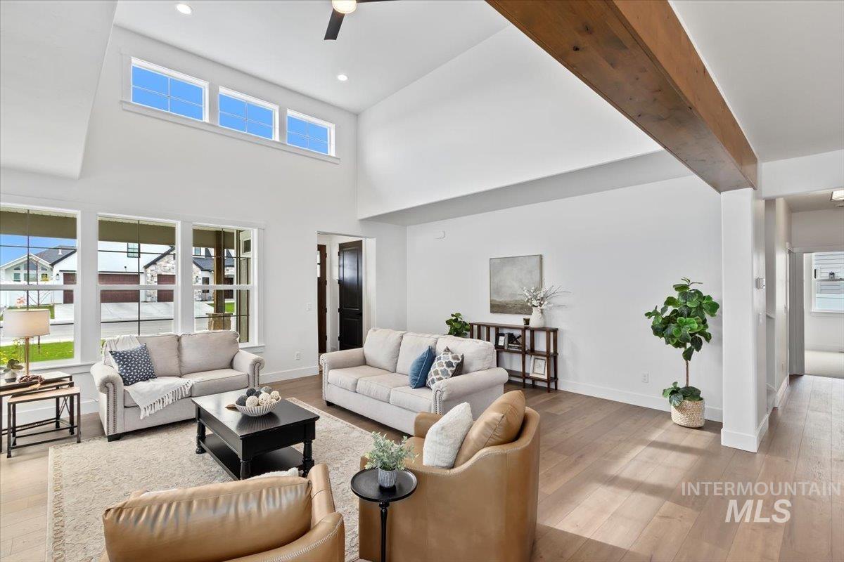 Living room featuring light wood-type flooring, beam ceiling, a towering ceiling, a ceiling fan, and recessed lighting