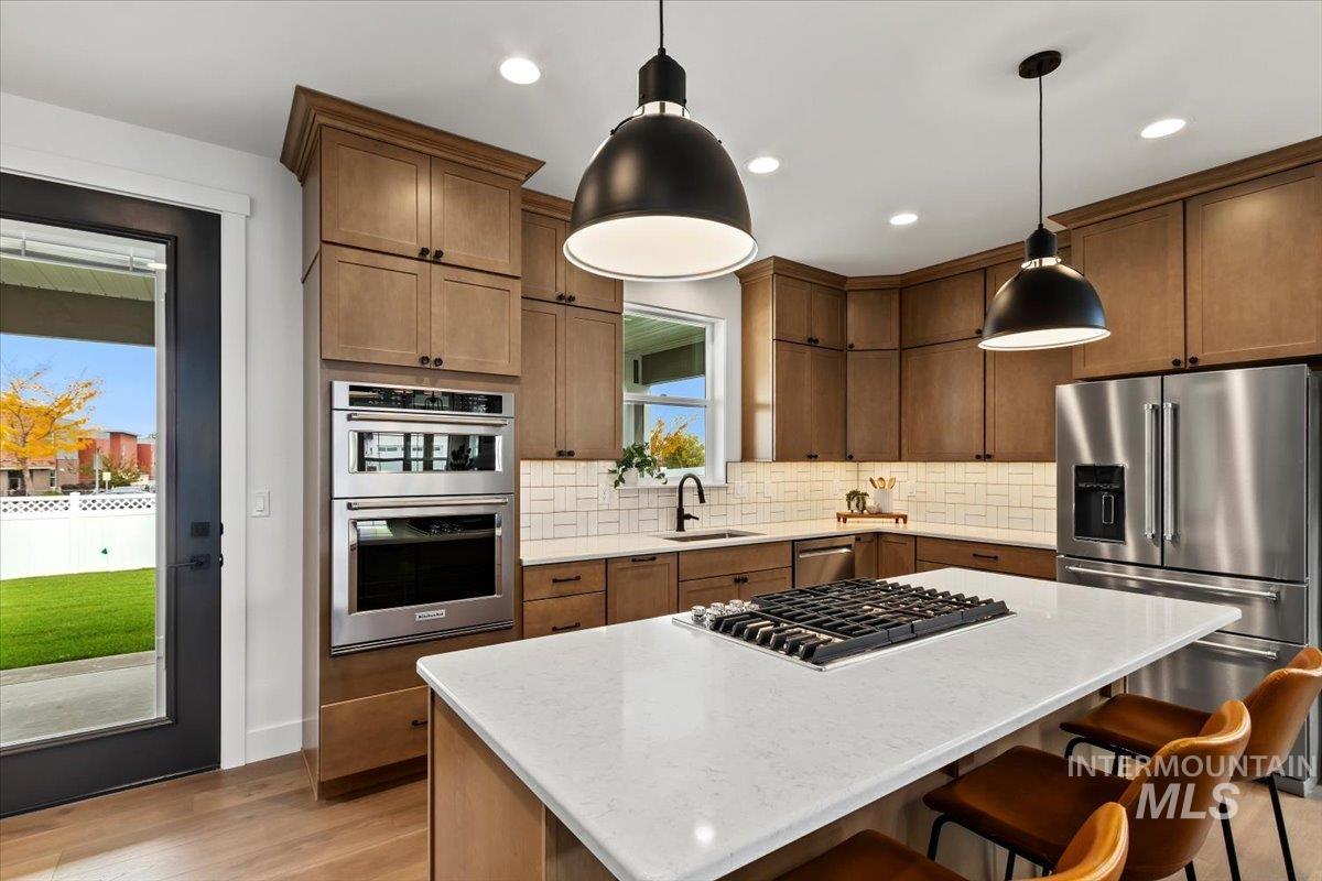 Kitchen with stainless steel appliances, light stone counters, a kitchen island, tasteful backsplash, and light wood finished floors