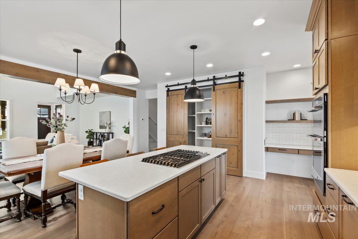 Kitchen featuring a barn door, a kitchen island, decorative light fixtures, light wood-style flooring, and decorative backsplash
