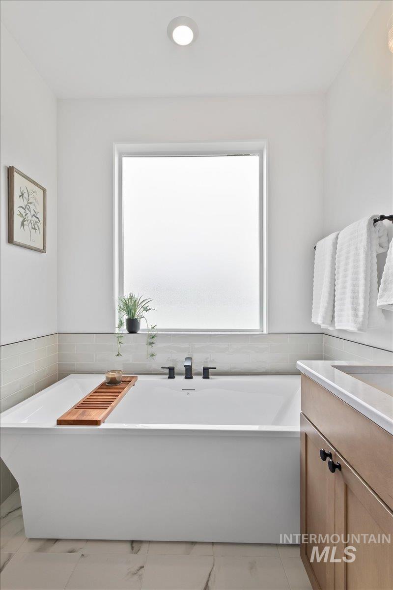 Bathroom with plenty of natural light, a freestanding tub, vanity, and tile walls