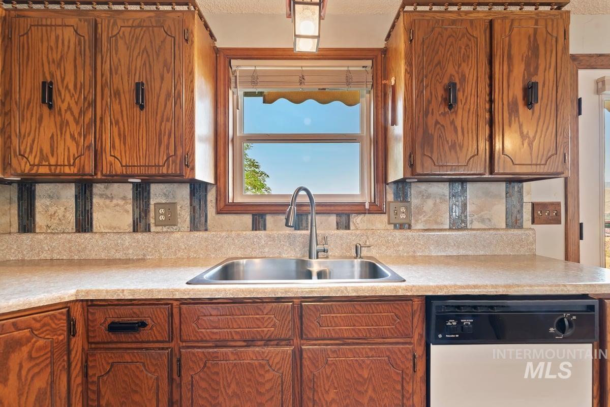 Kitchen with white dishwasher, light countertops, backsplash, brown cabinetry, and a textured ceiling