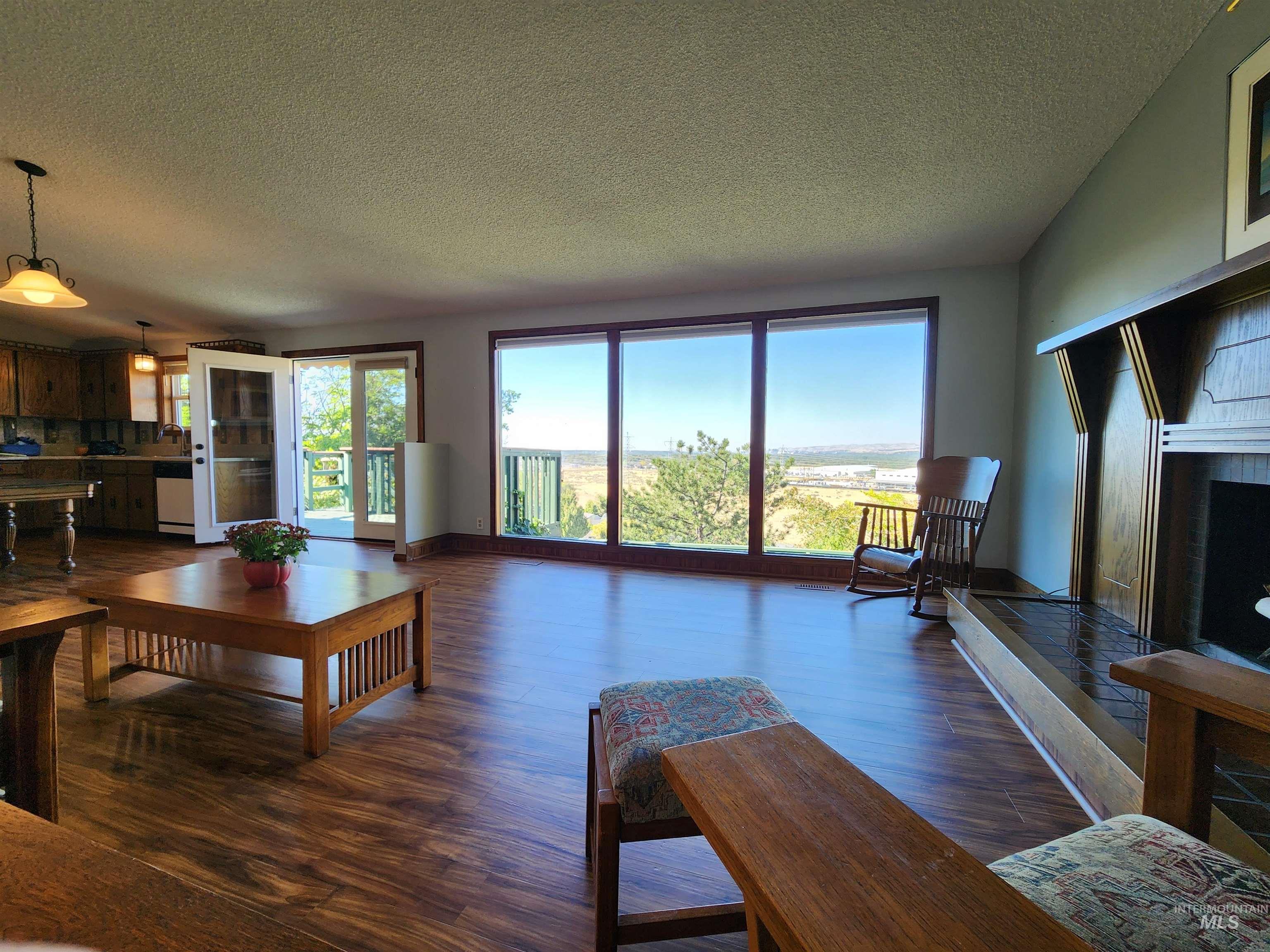 Living area with a textured ceiling, dark wood-style flooring, and a fireplace with raised hearth