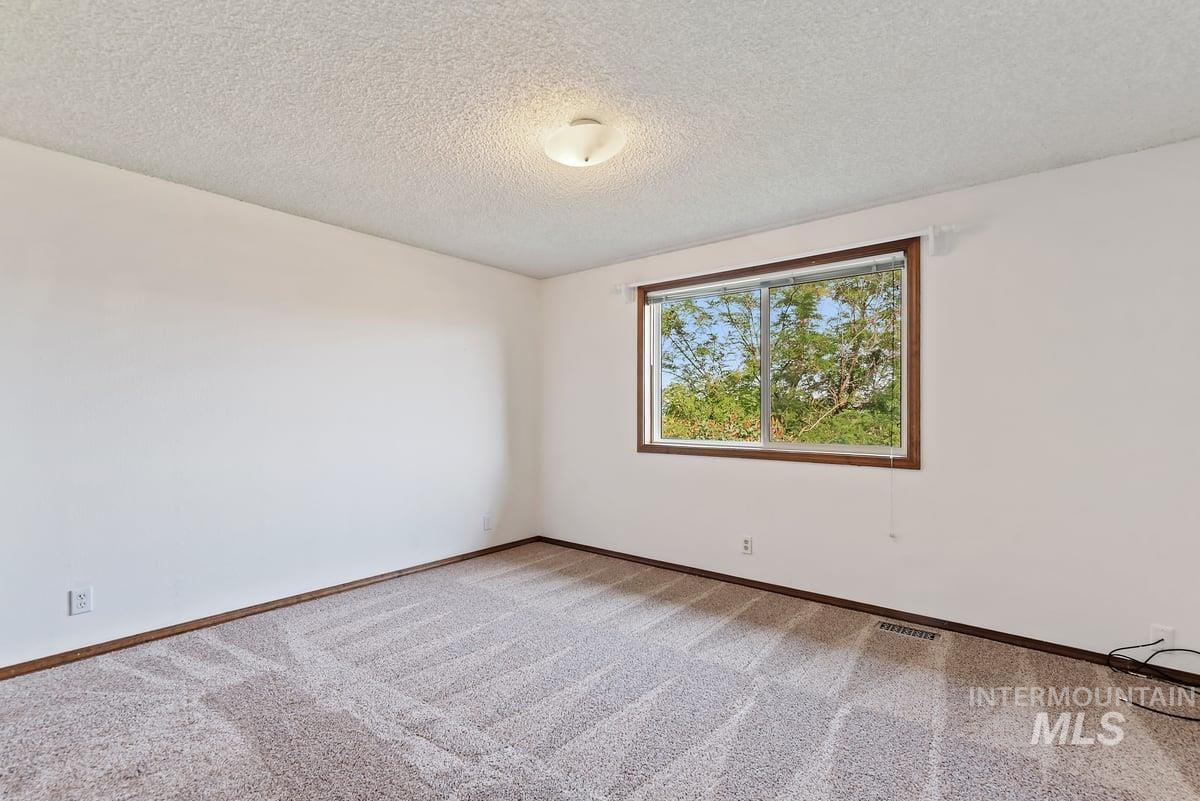 Carpeted empty room with a textured ceiling and baseboards