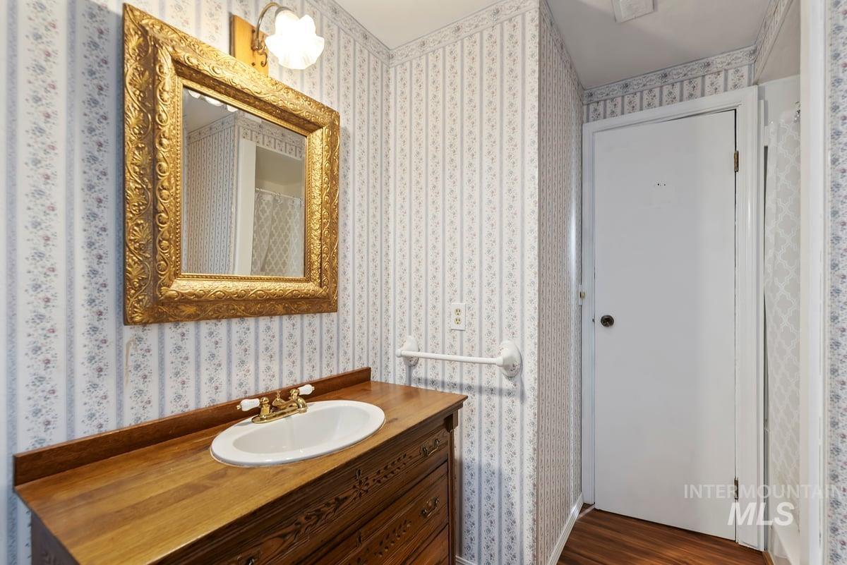 Full bath with vanity, wallpapered walls, and dark wood-style floors