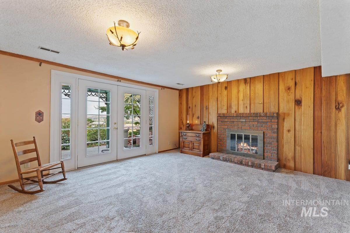Unfurnished living room featuring wood walls, french doors, a fireplace, carpet, and a textured ceiling