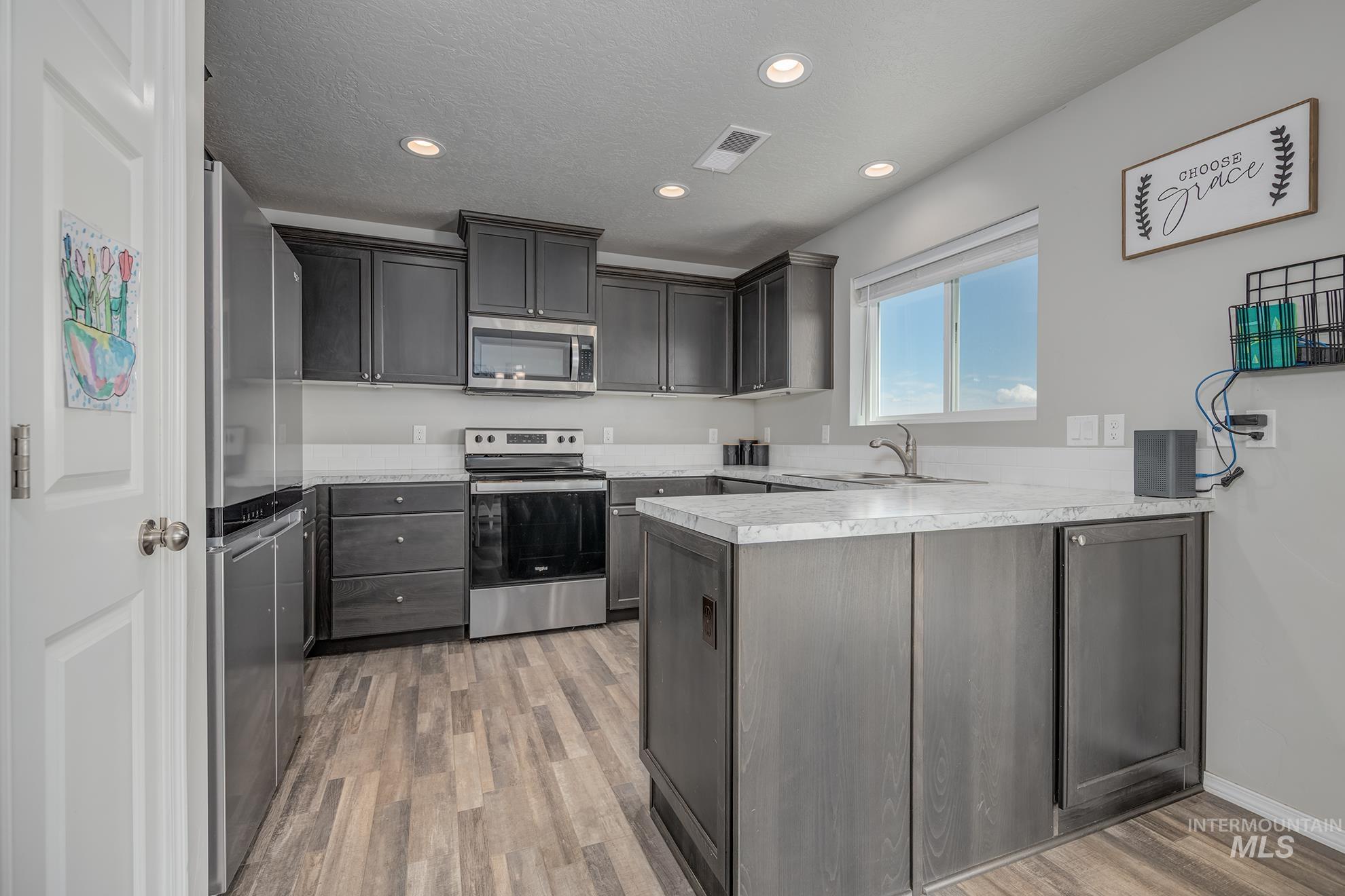 Modern kitchen featuring dark wood-finish cabinetry, stainless steel appliances, light-toned countertops, and recessed lighting