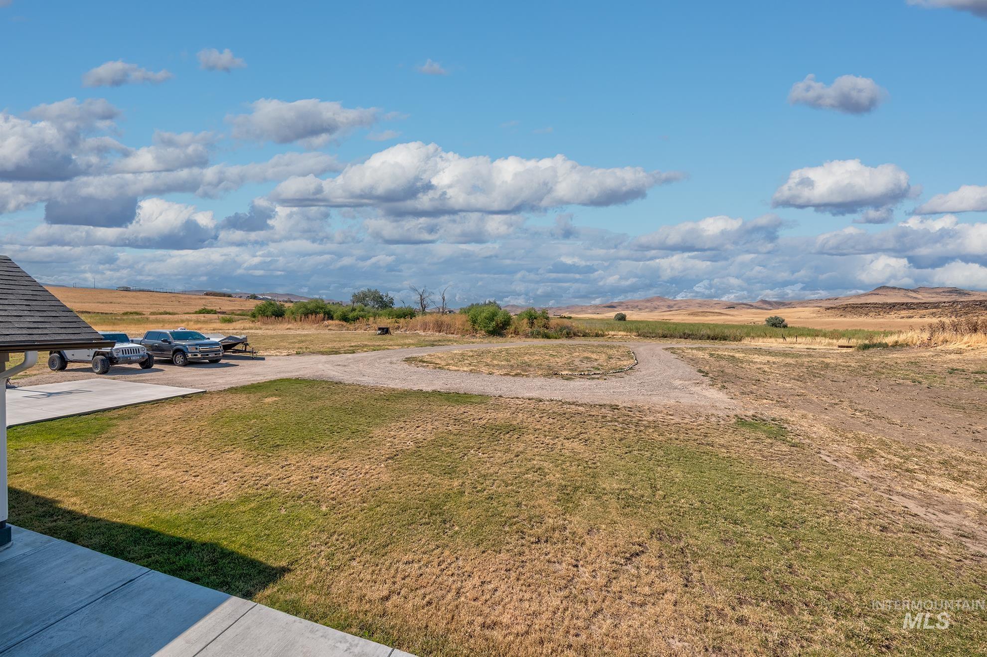 Expansive rural landscape featuring a gravel driveway, natural terrain, and distant hills