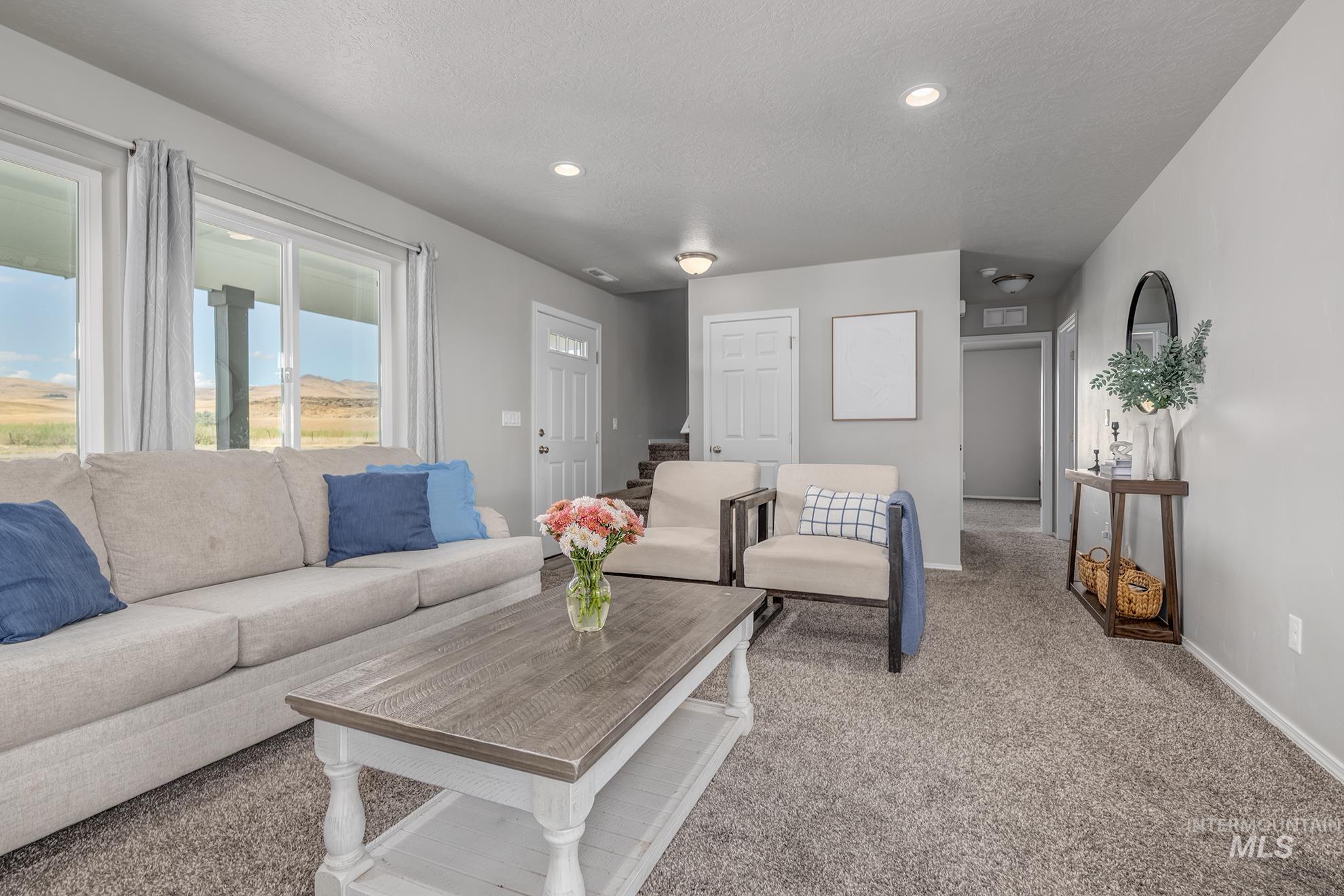 Living area featuring light gray wall paint, gray carpeting, recessed ceiling lighting, and large sliding glass doors opening to outdoor scenery