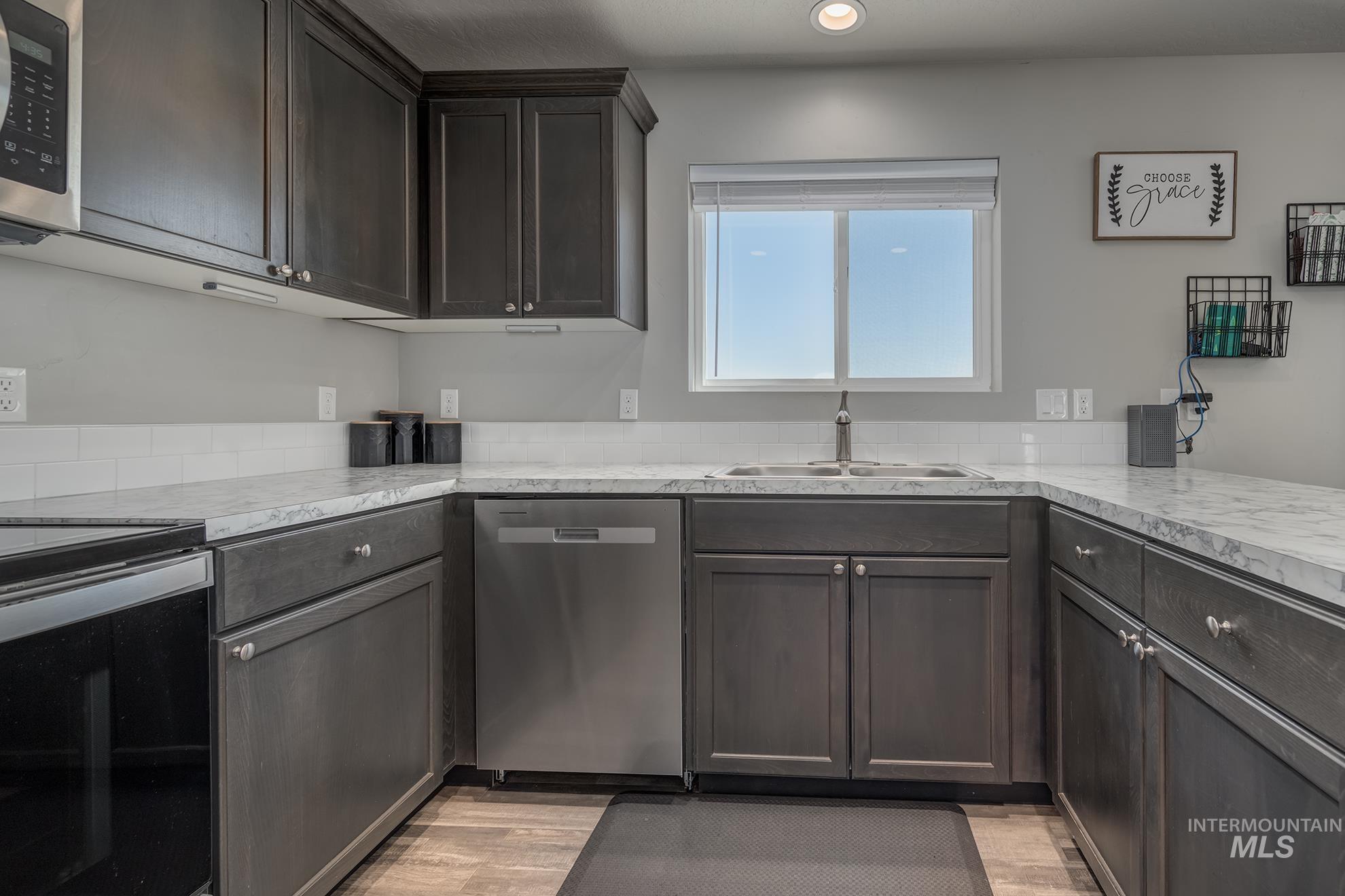 Kitchen featuring dark wood-finish cabinetry, light-toned countertops, subway tile backsplash, stainless steel appliances, and wood-finish flooring